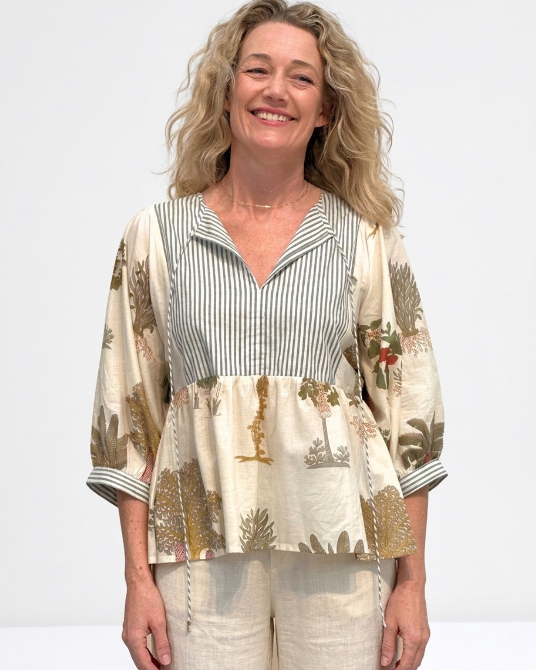 Woman wearing the Reca Botanica Luxe Cotton Blouse, a cream botanical print blouse with a sage and white striped bodice panel, styled with linen pants