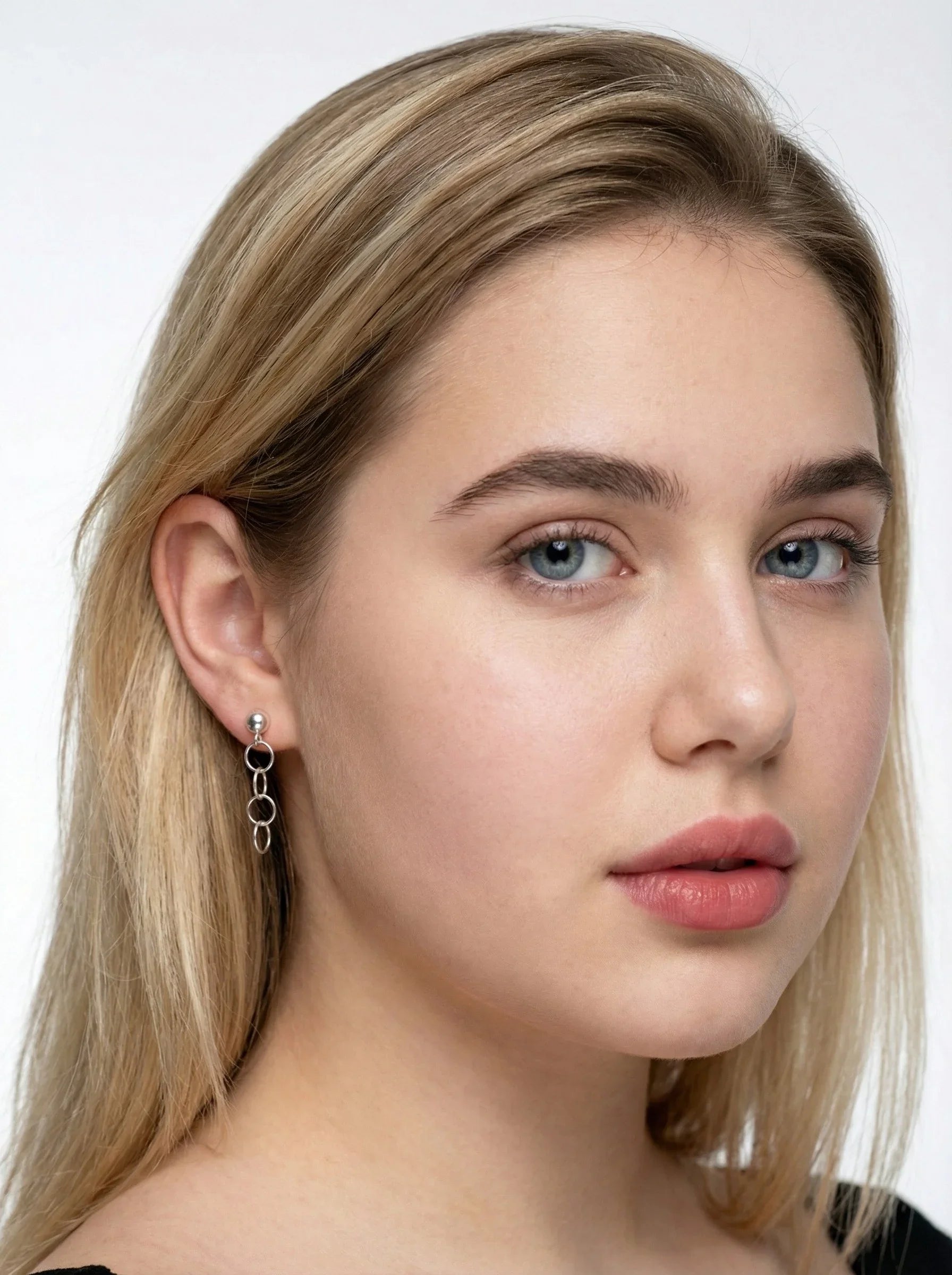 Close-up of a model wearing earrings from Reca - with blonde hair wearing Silver Oval Chain Drop Earrings on a white background
