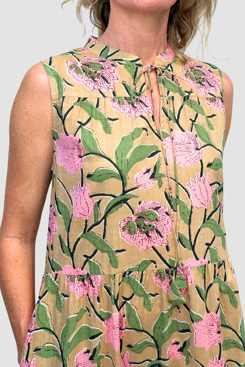 Woman wearing a sleeveless dress with pink floral pattern on a plain background