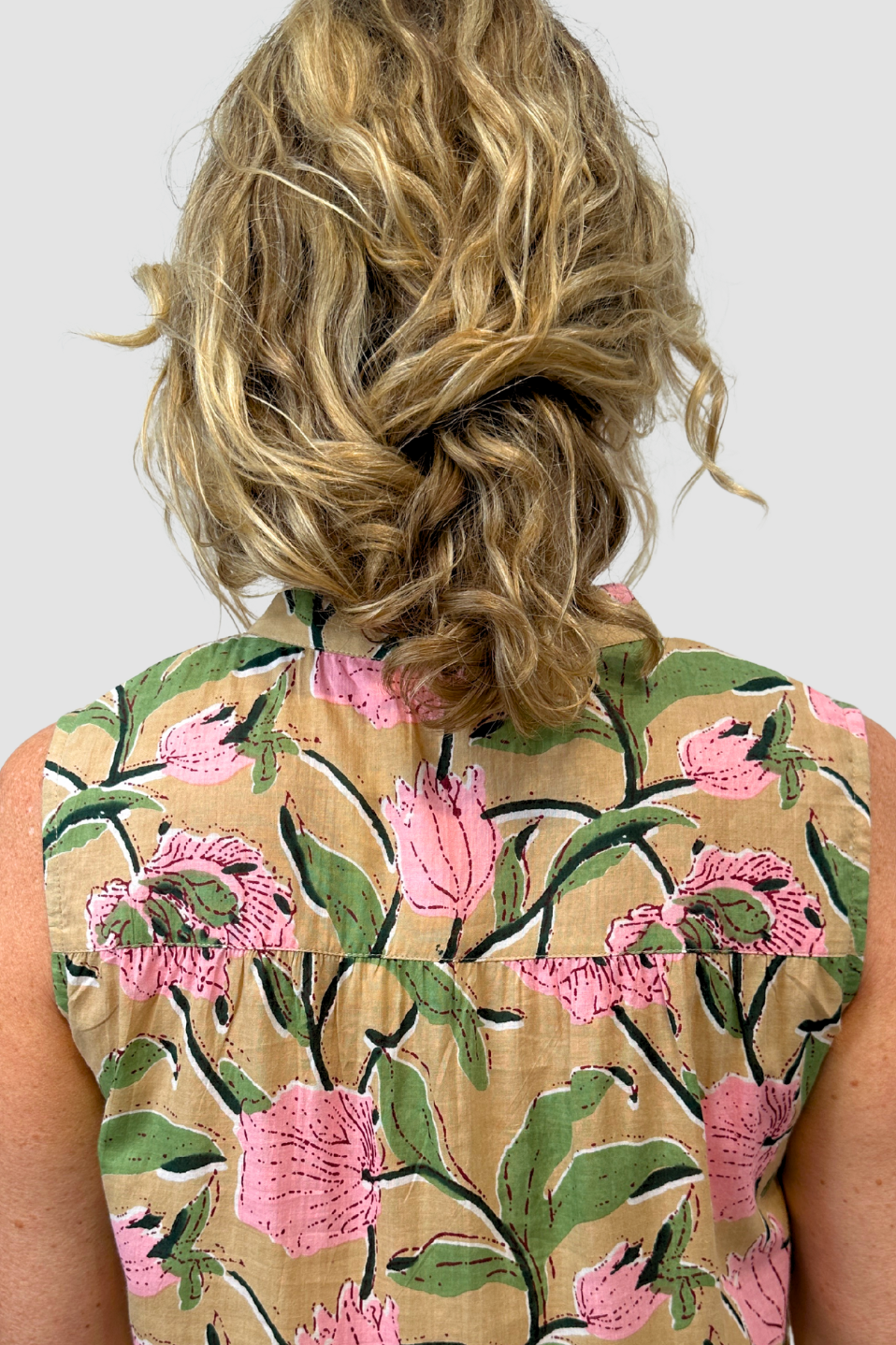 Person wearing a sleeveless top with floral pattern on a plain background