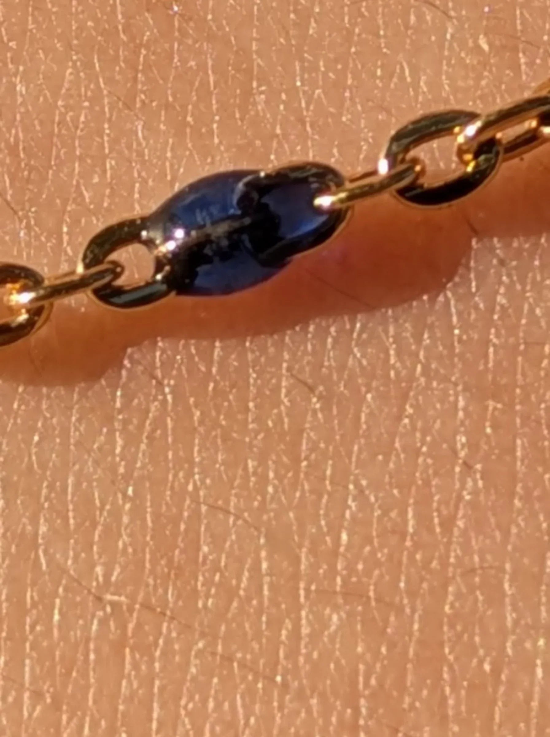 Close-up of a gold chain with a small blue stone, Reca ethical jewellery detail