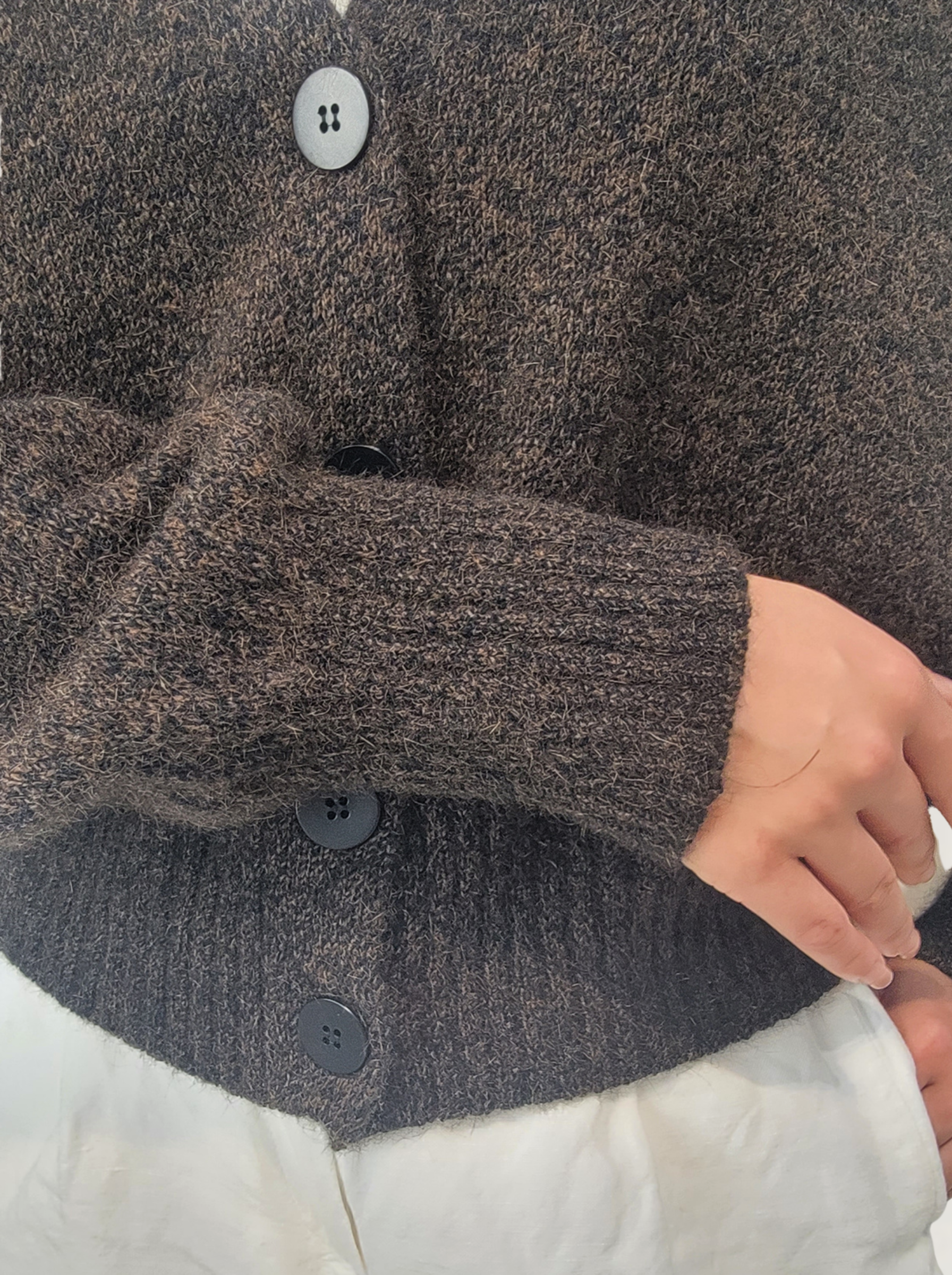 Close-up of a person wearing V-Neck Cardigan - Brown Marl with buttons, holding a white object.