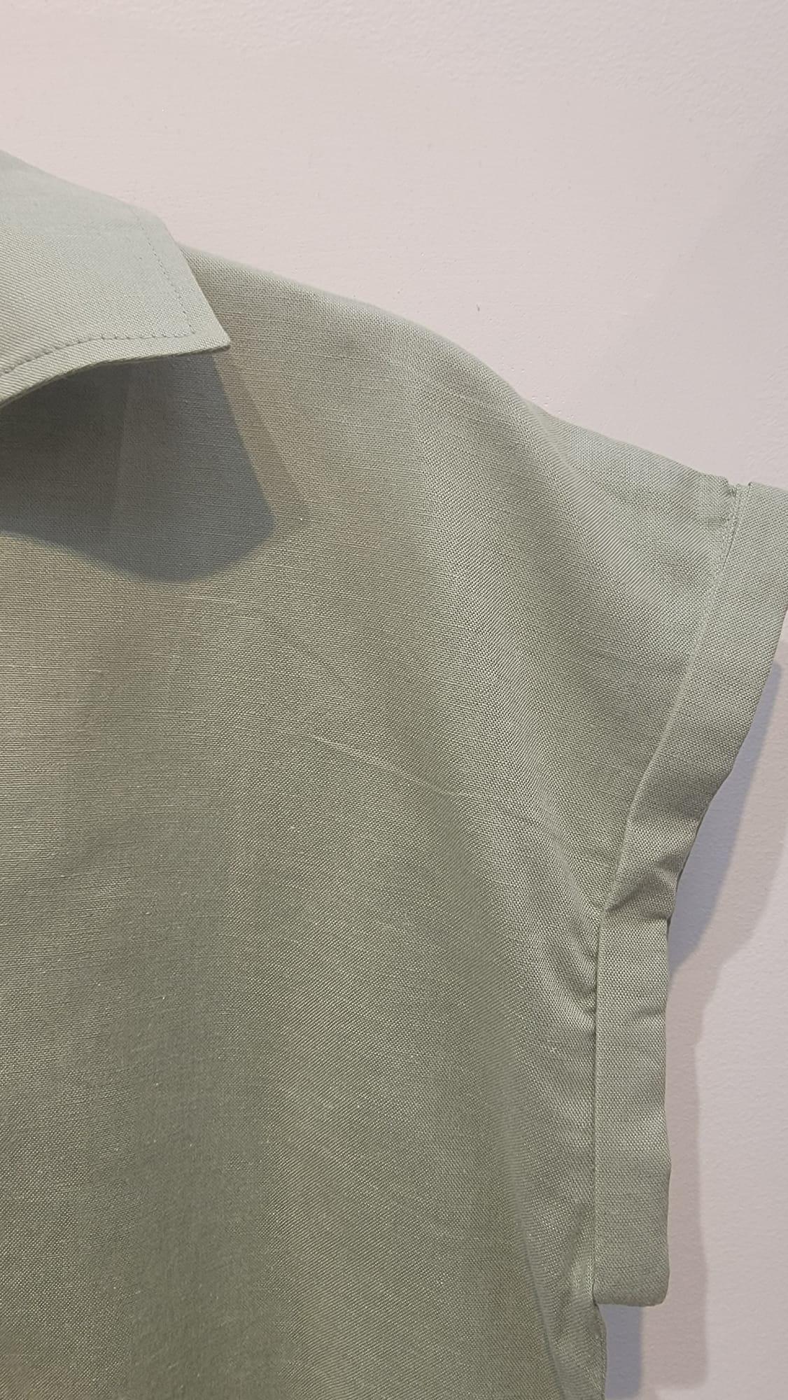 Close-up of an ethical light green linen shirt sleeve from Reca against a pale wall