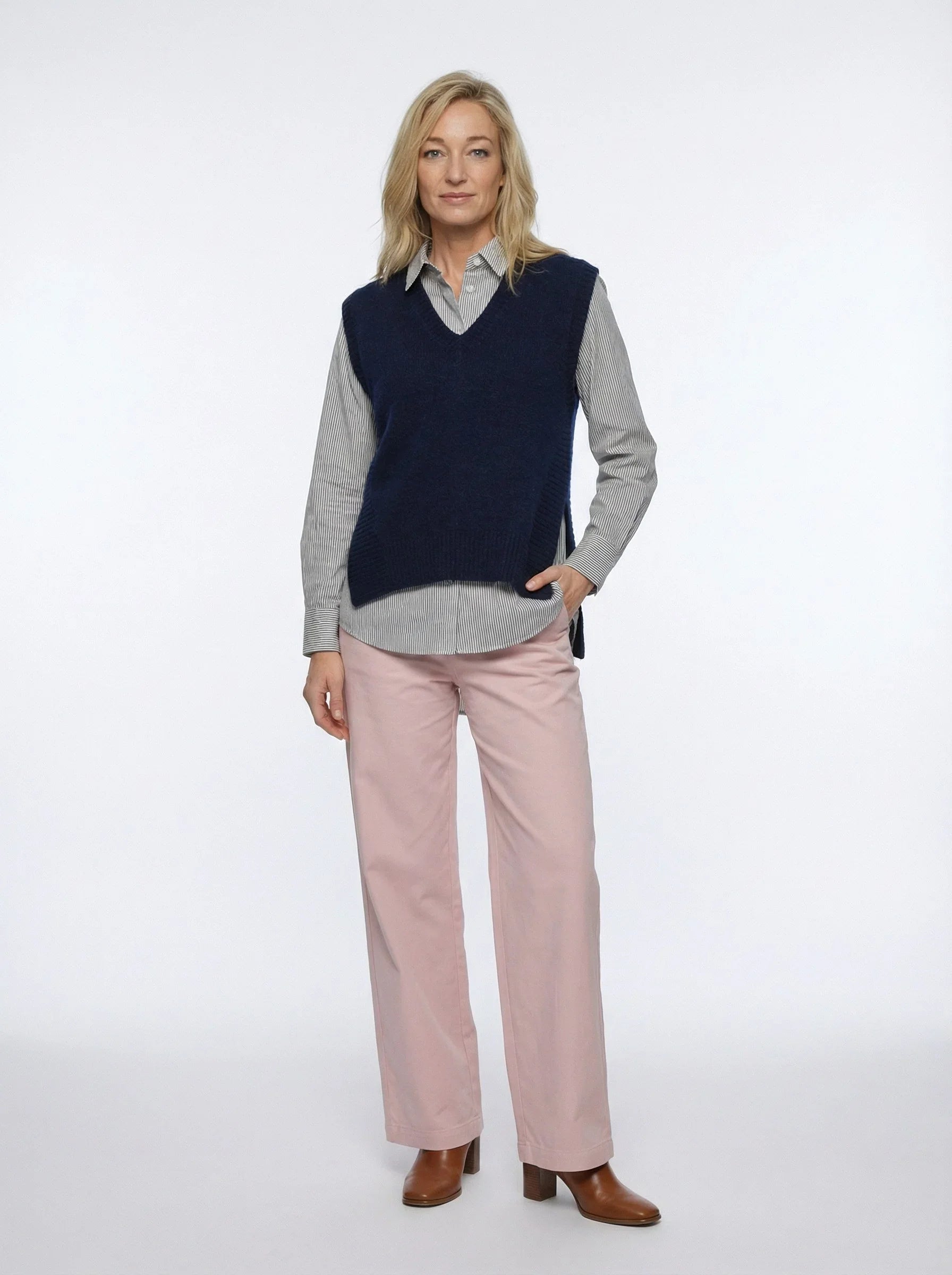 Woman wearing navy knit vest over striped shirt with light pink wide-leg trousers and brown boots