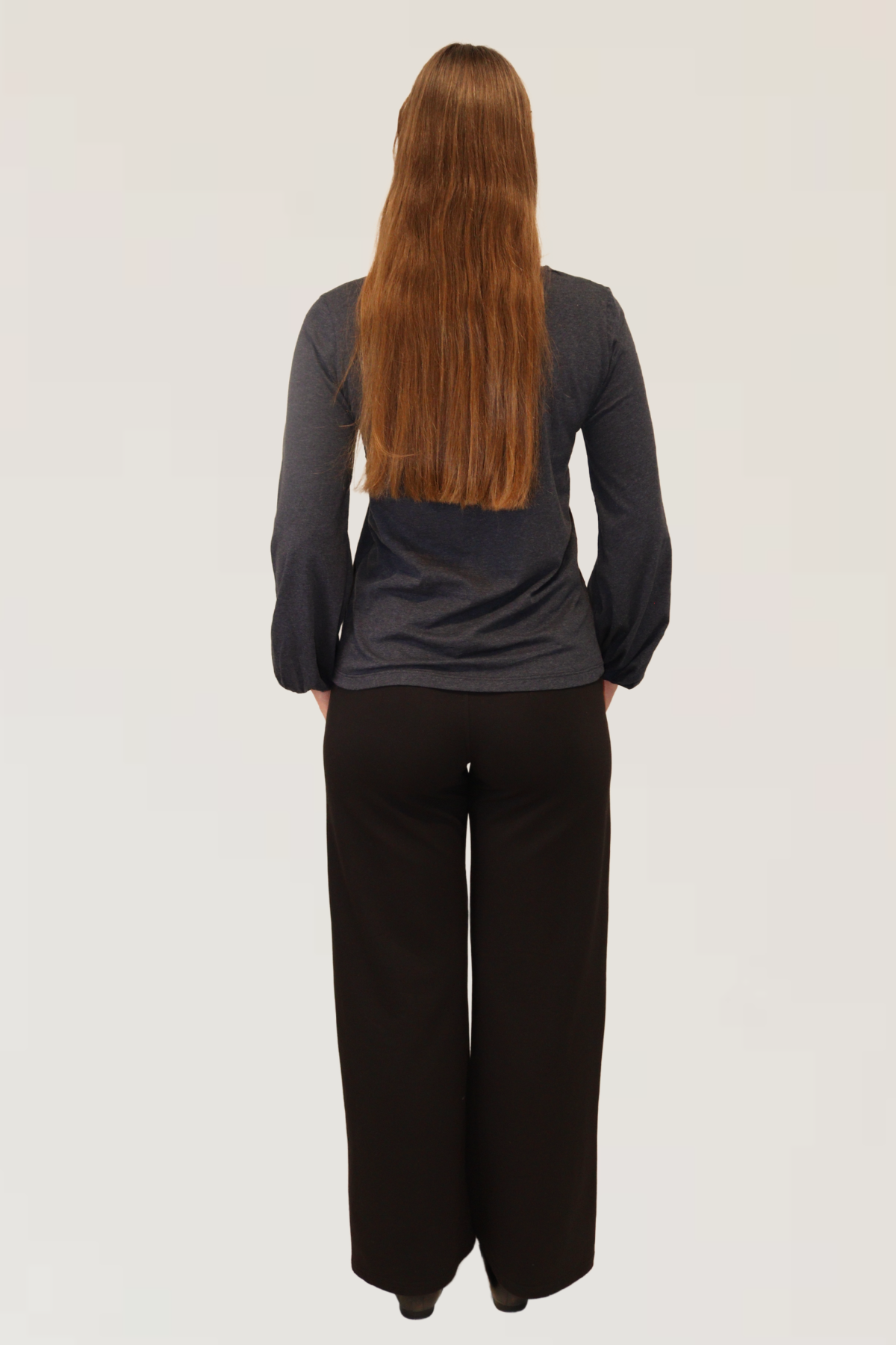 Back view of Reca Bishop Blouse in Ink, long sleeves with gathered cuffs, paired with black drape trousers.