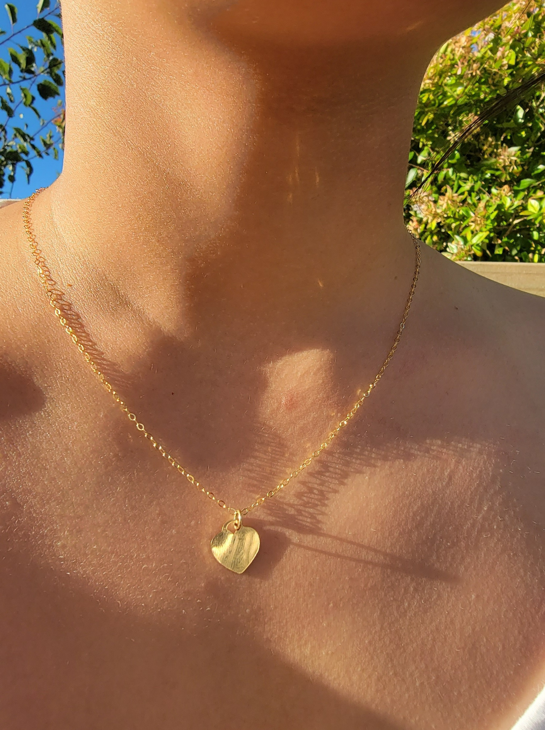 Gold necklace with a heart pendant on a person against a natural background