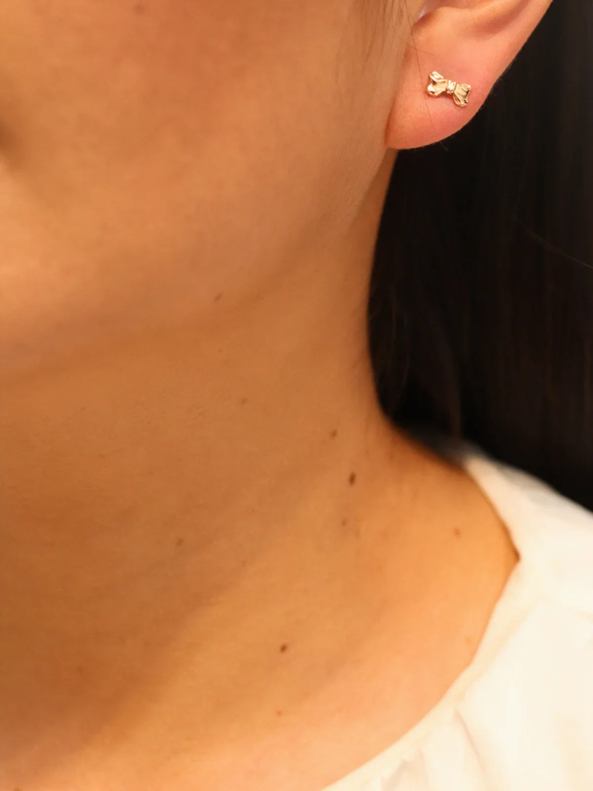 Gold bow stud earring, worn on ear.