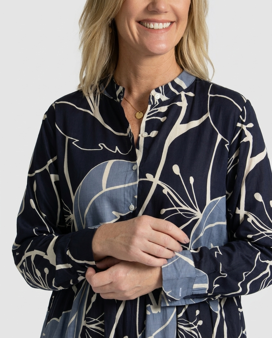 Close-up of the Indigo Bloom cotton midi dress showing the band collar, buttoned placket and long sleeve cuff in cream and dusty-blue botanical print on navy