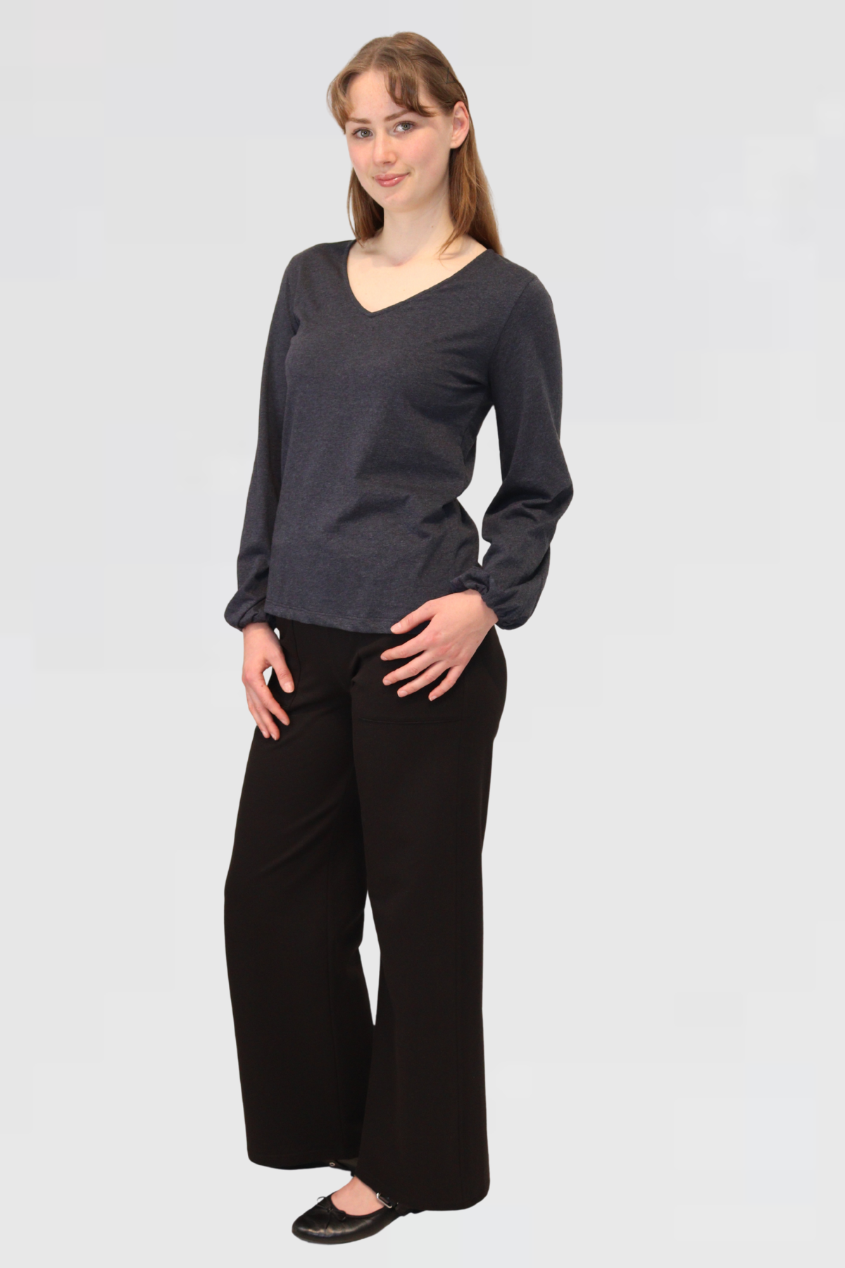 Model wearing Reca Bishop Blouse in Ink with V-neckline and long bishop sleeves, styled with black trousers, angled view.