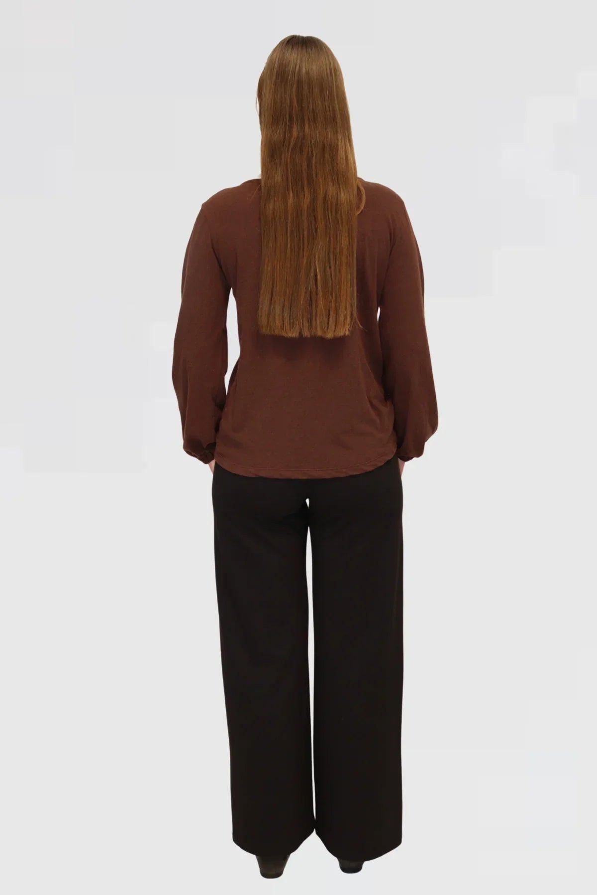 Back view of Reca Bishop Blouse in Redwood, long sleeves and relaxed silhouette paired with black trousers.