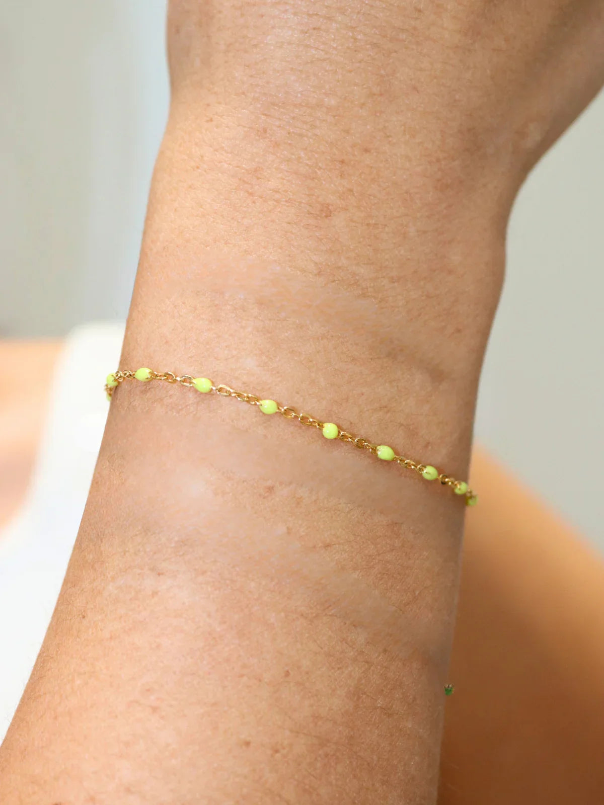 Gold bracelet with yellow stone on a person's ankle against a neutral background