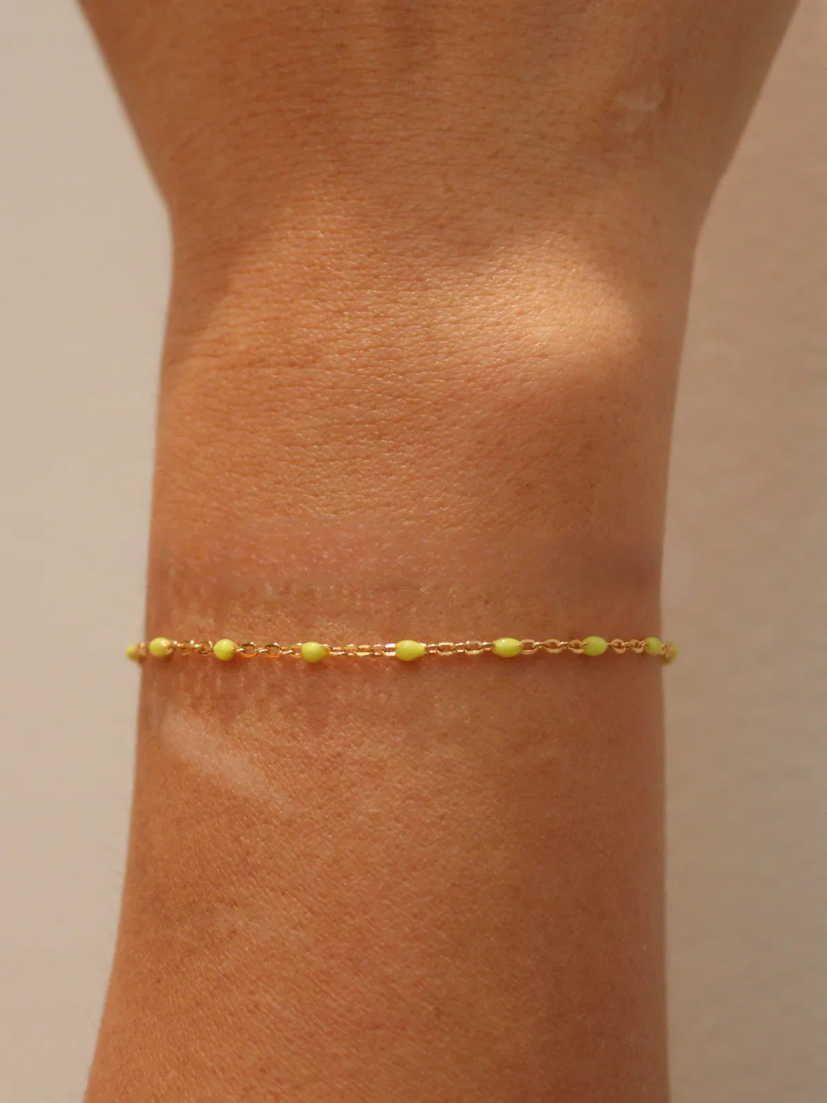 Gold bracelet with yellow beads on a person's ankle against a neutral background