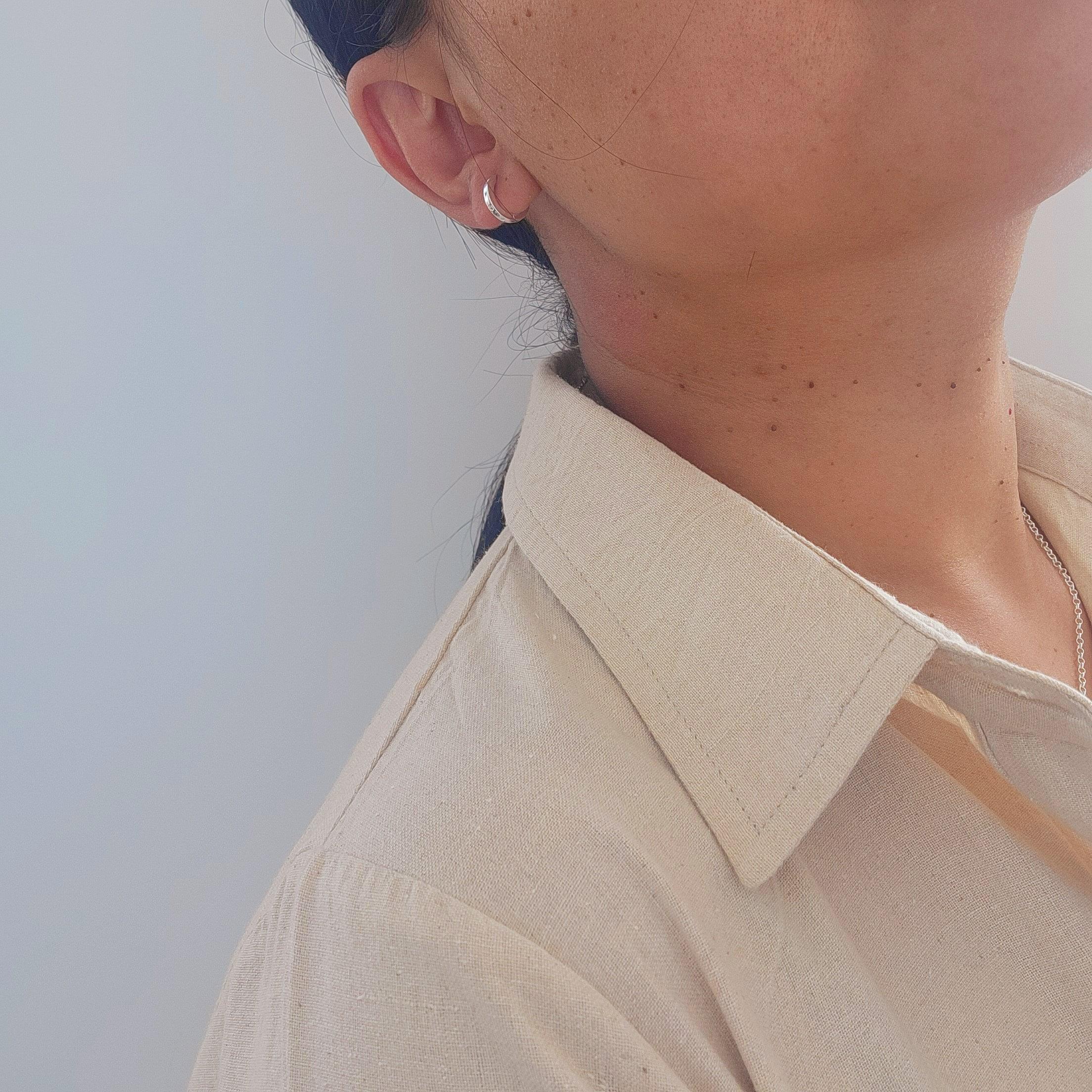 Close-up of an ear with a silver hoop sleeper earring against a neutral background