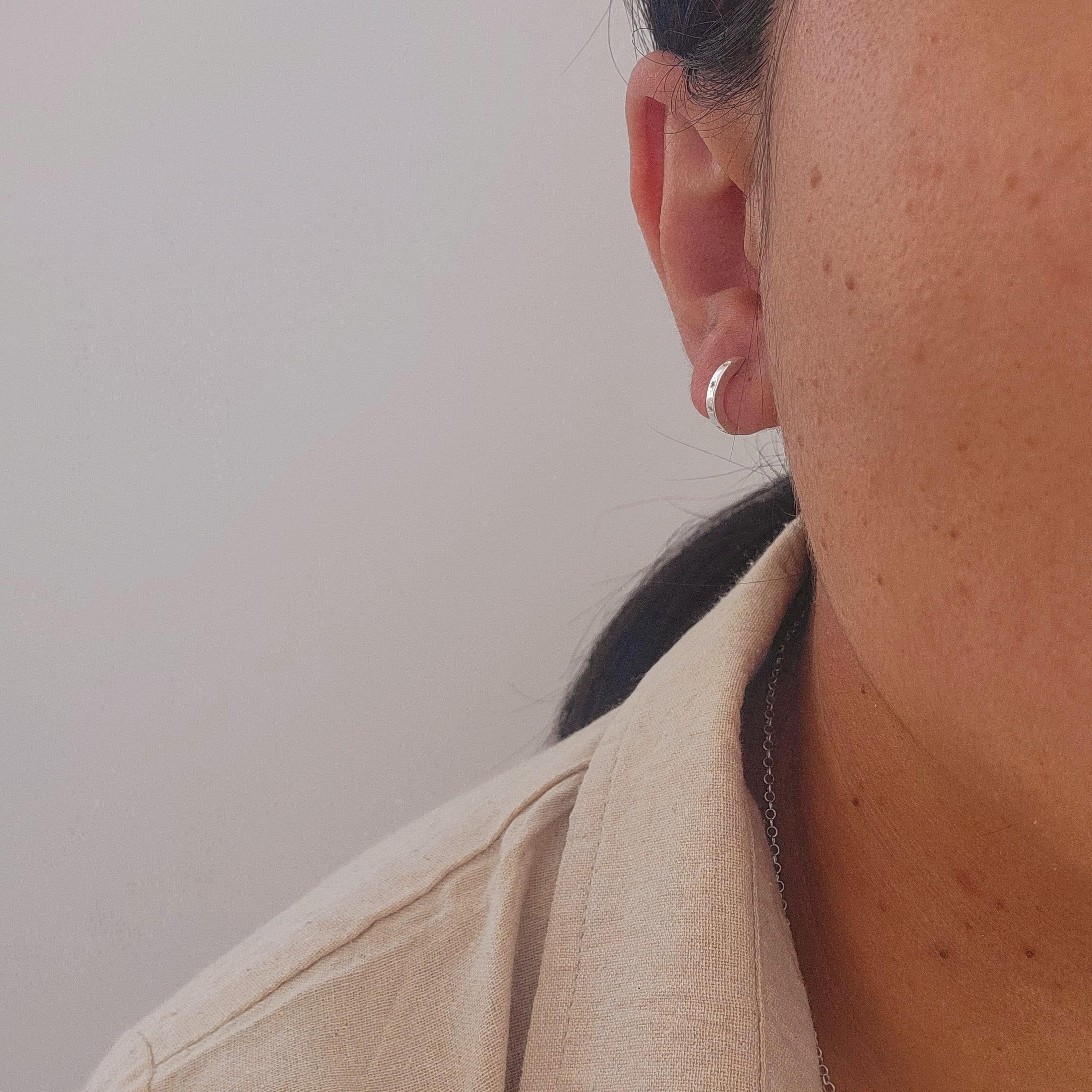 Close-up of an ear with a silver hoop sleeper earring against a neutral background