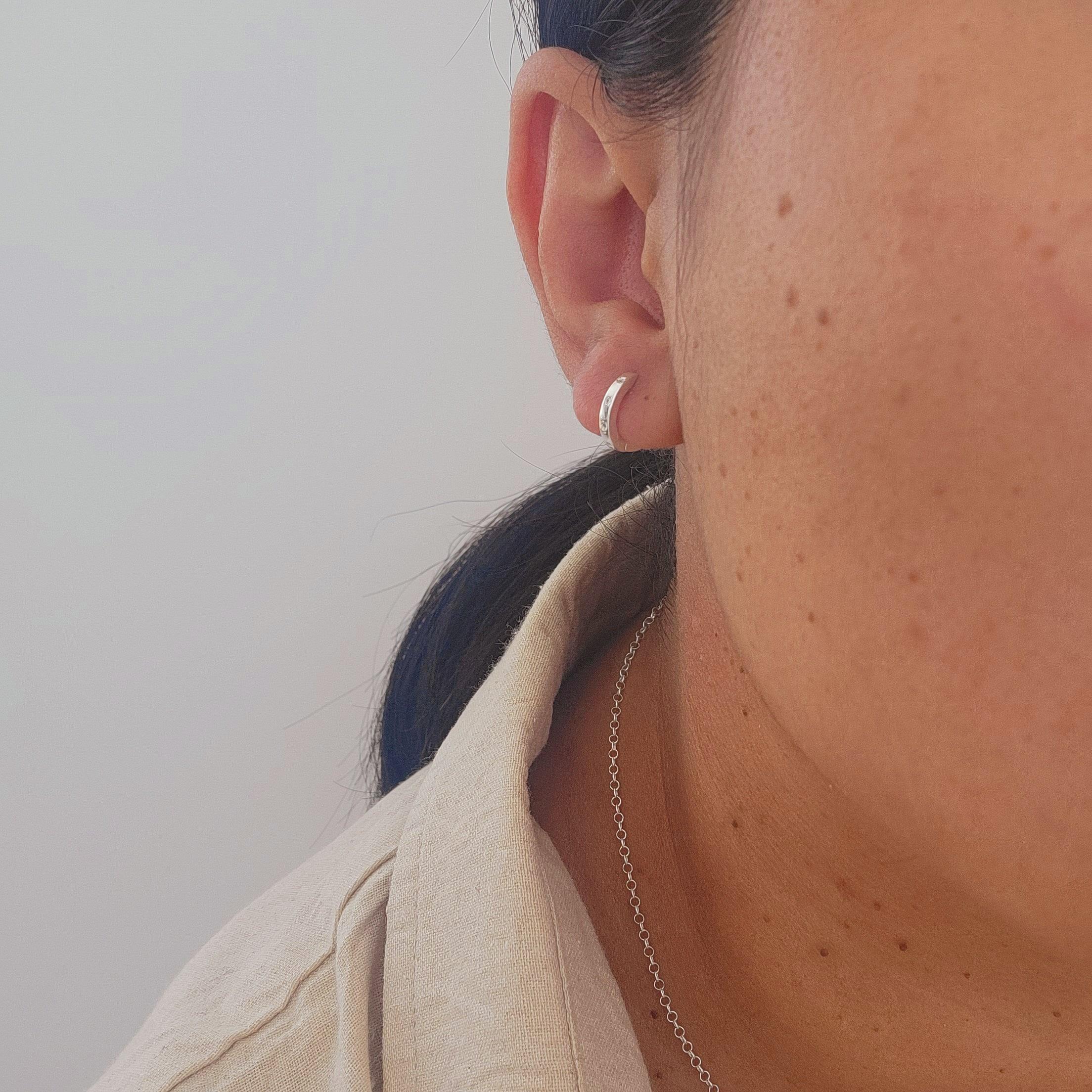 Close-up of an ear with a silver hoop sleeper earring against a neutral background