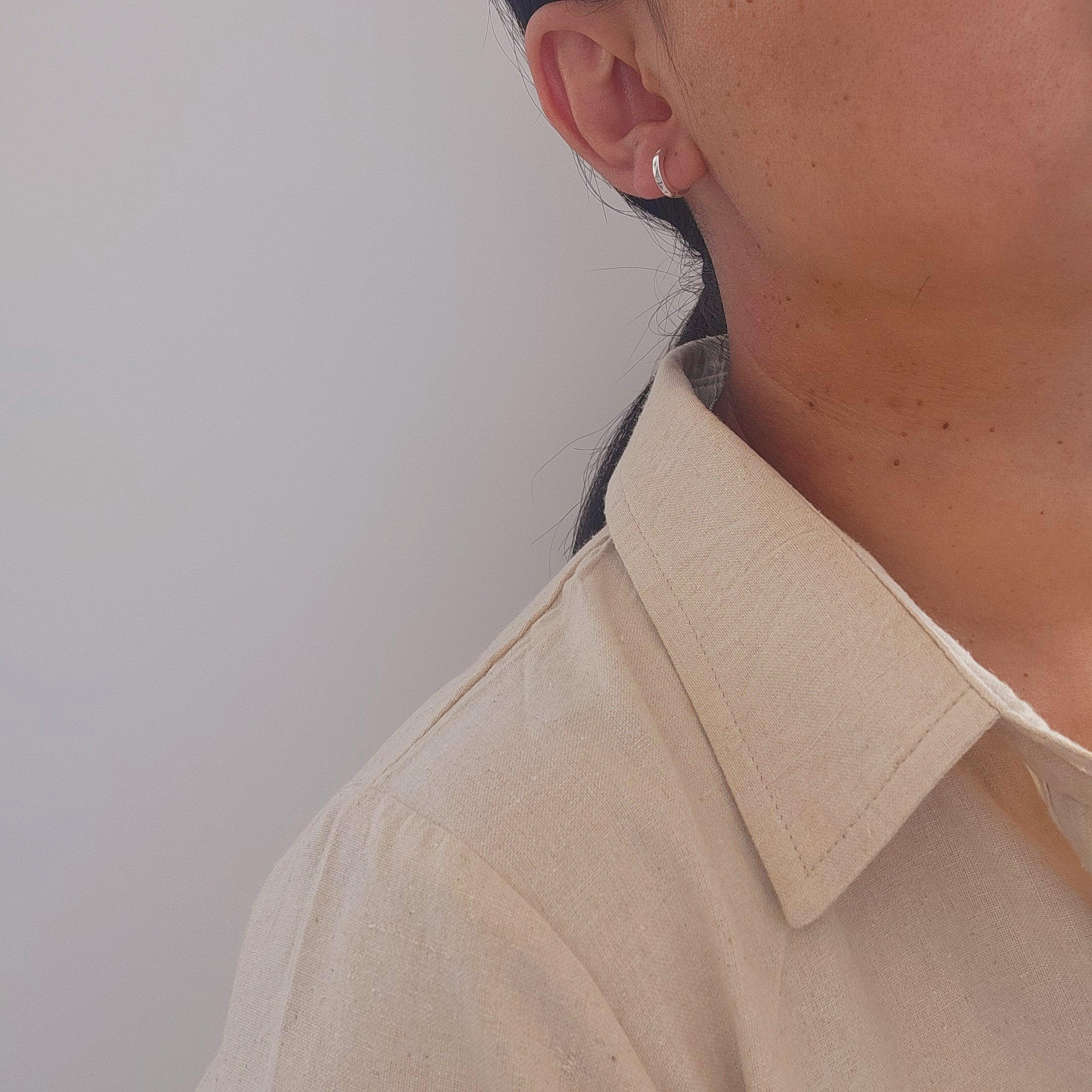 Close-up of an ear with a silver hoop sleeper earring against a neutral background