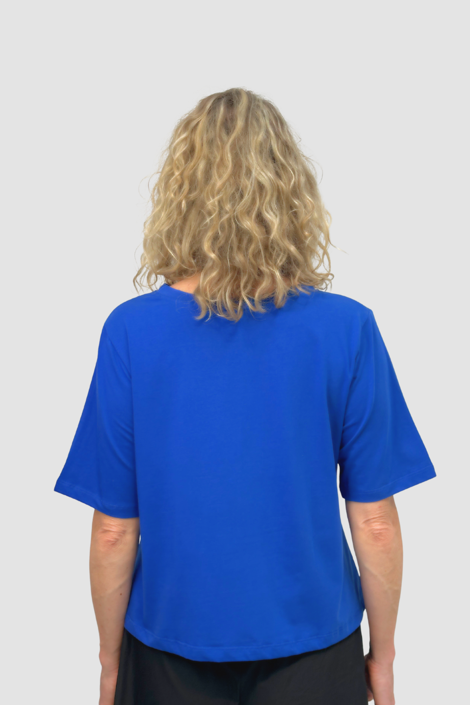 Back view of person with curly blonde hair wearing bright blue short-sleeve shirt on gray background