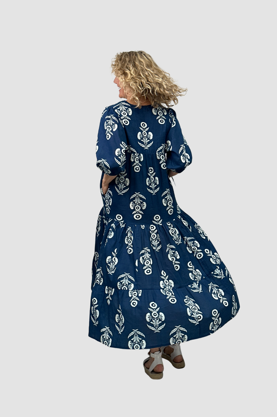 Woman wearing a long blue dress with white floral pattern on a white background