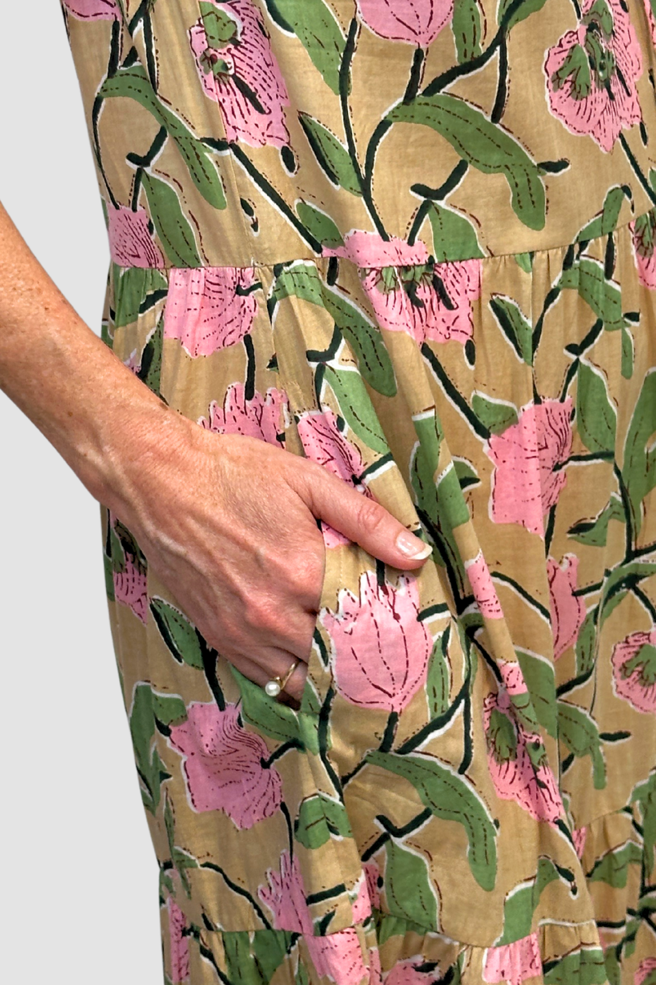 Close-up of a floral patterned dress with pink flowers and green leaves on a beige background.