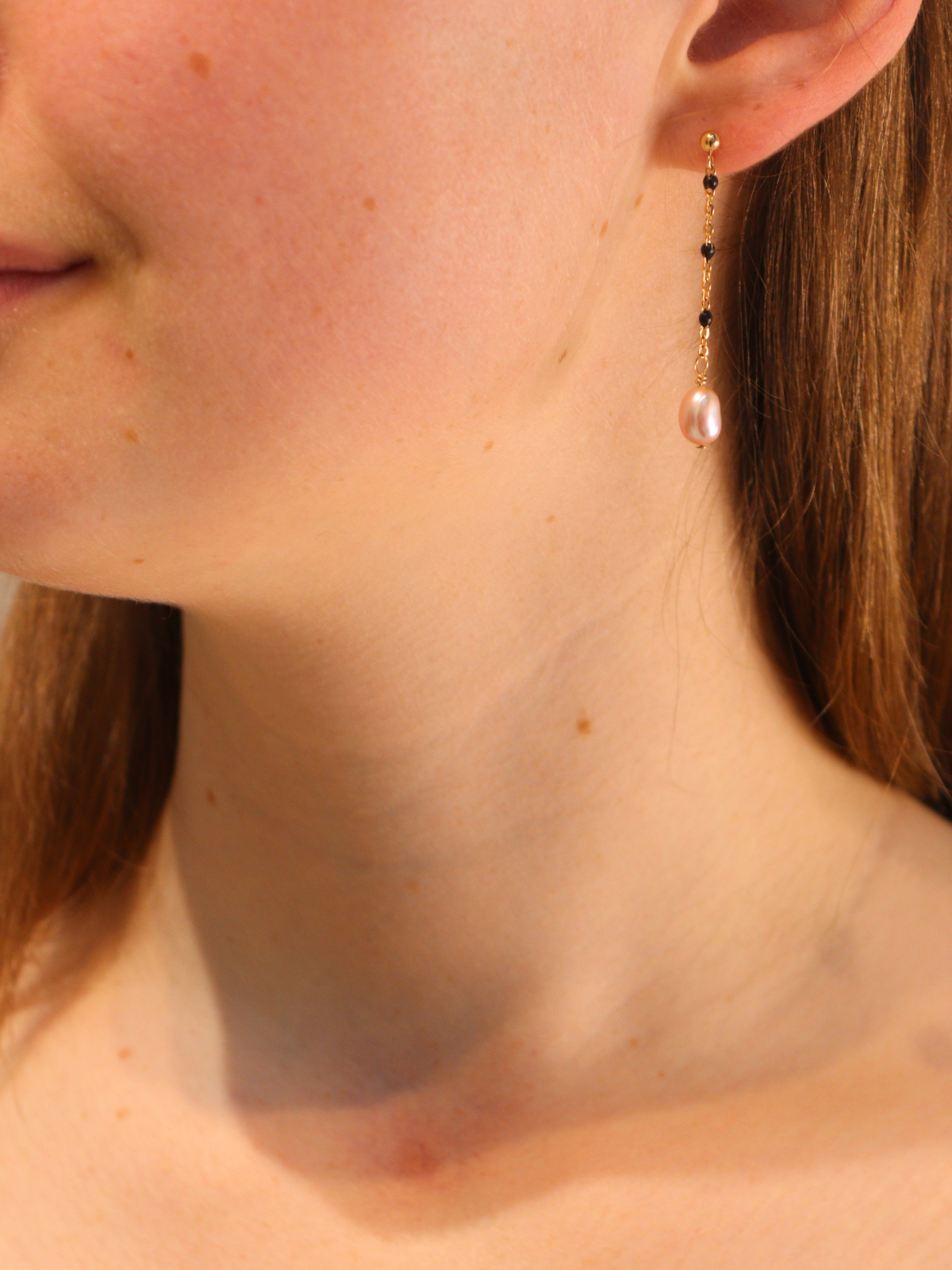 Gold chain link drop earring with pearl pendant, worn on ear.