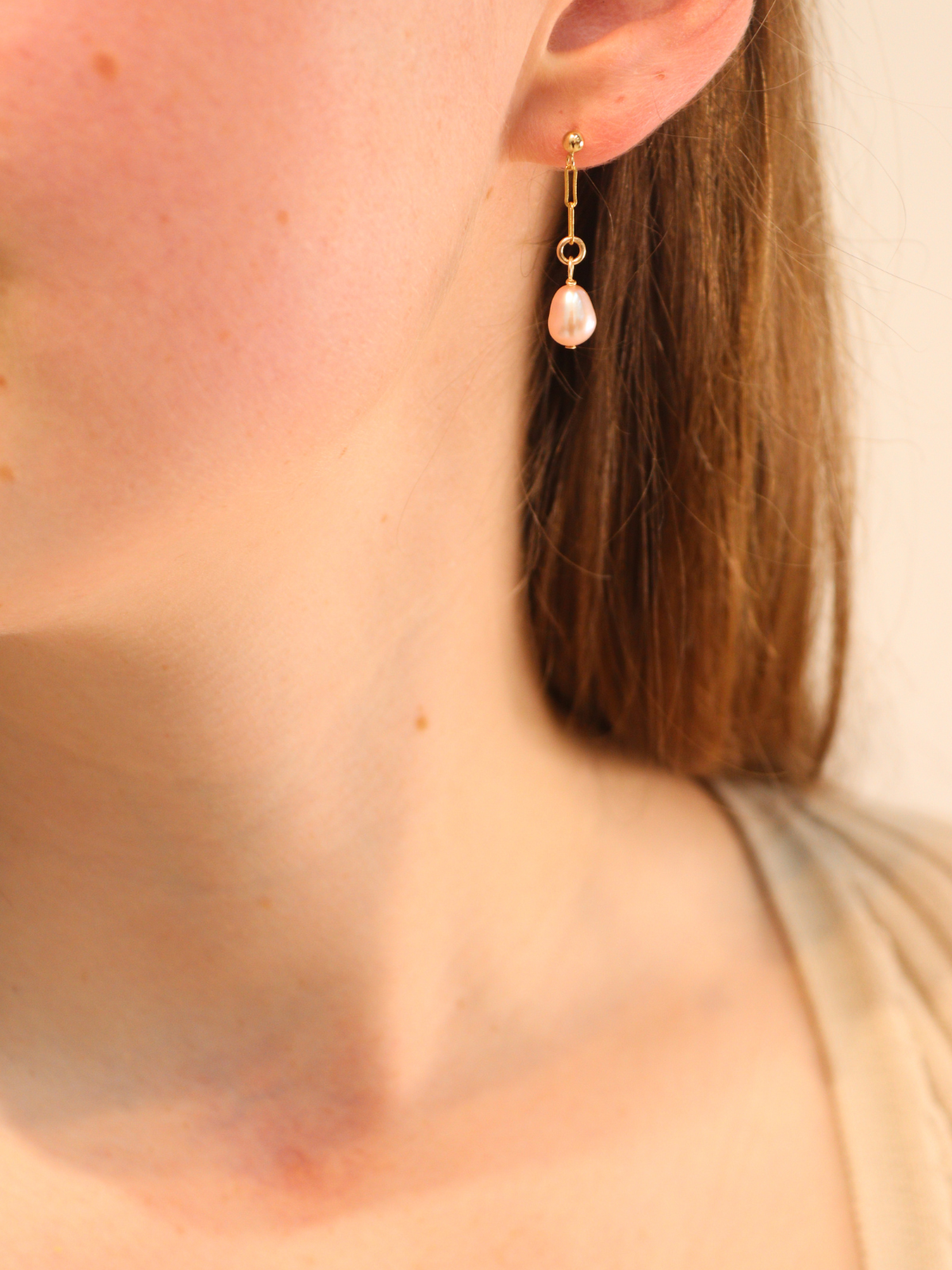 Gold link drop earring with teardrop white pearl pendant, worn on ear.