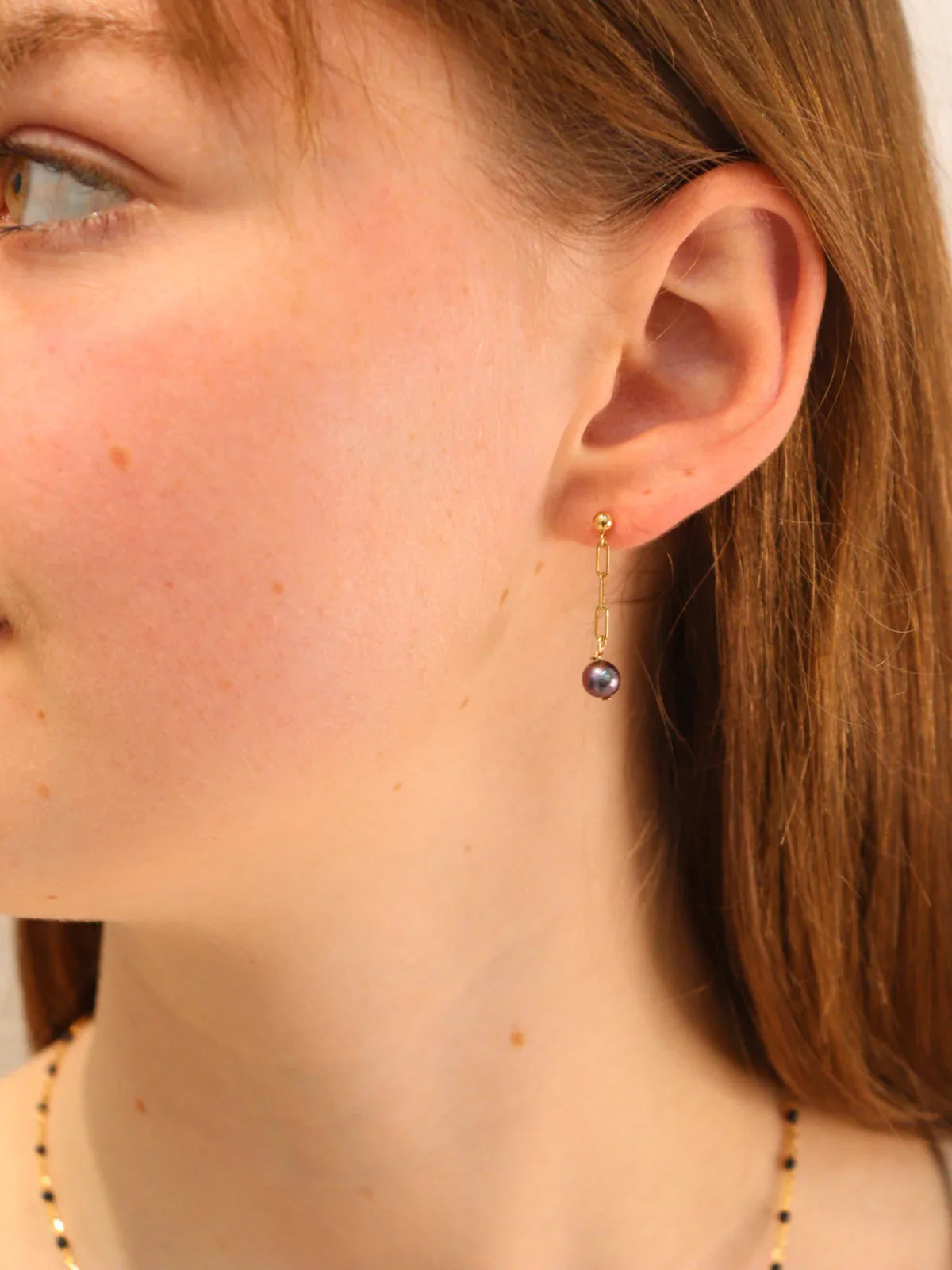 Woman wearing elegant gold drop earrings with black pearl charm.