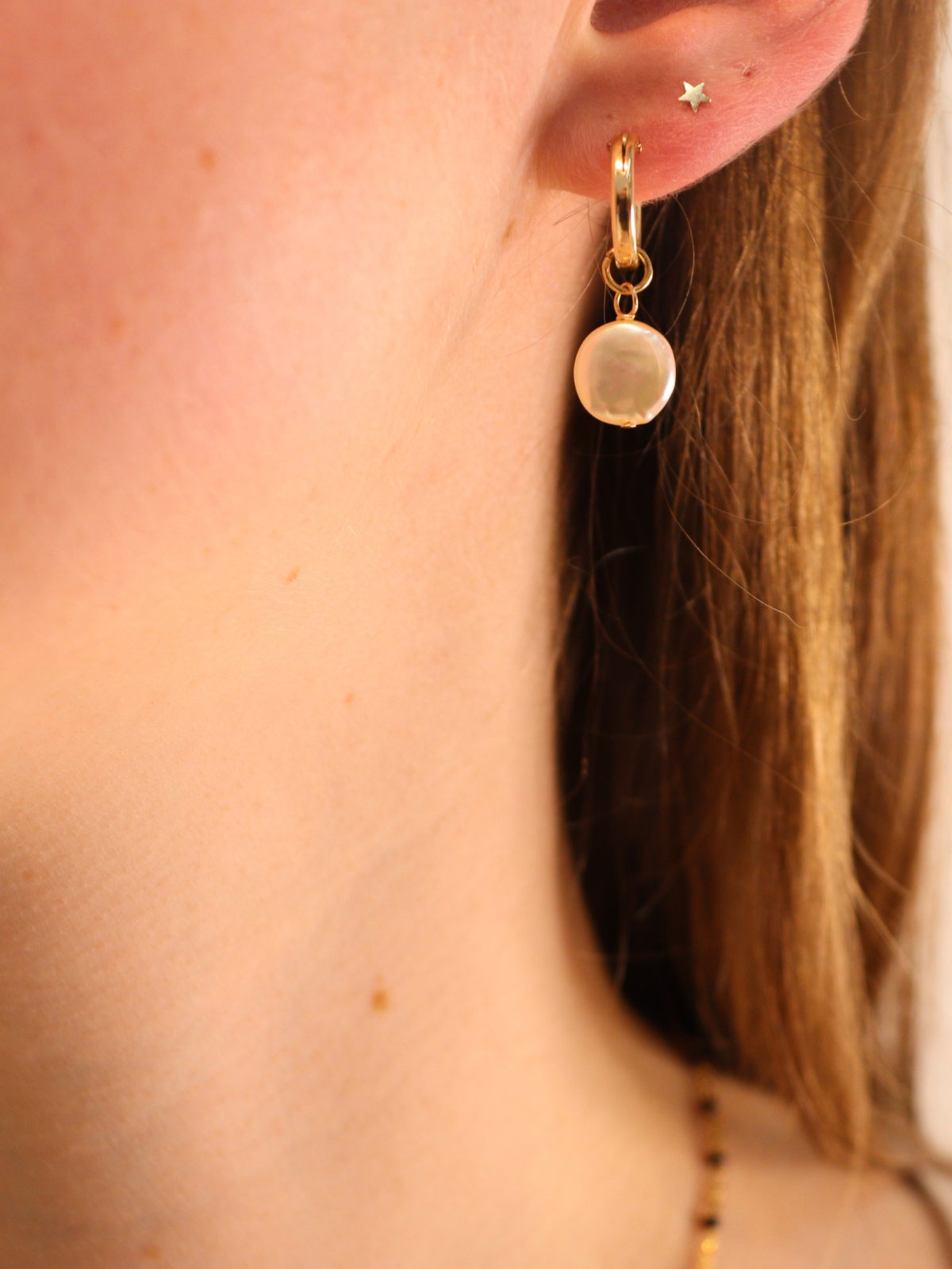 Gold hoop earring with coin pearl pendant, styled with star stud.