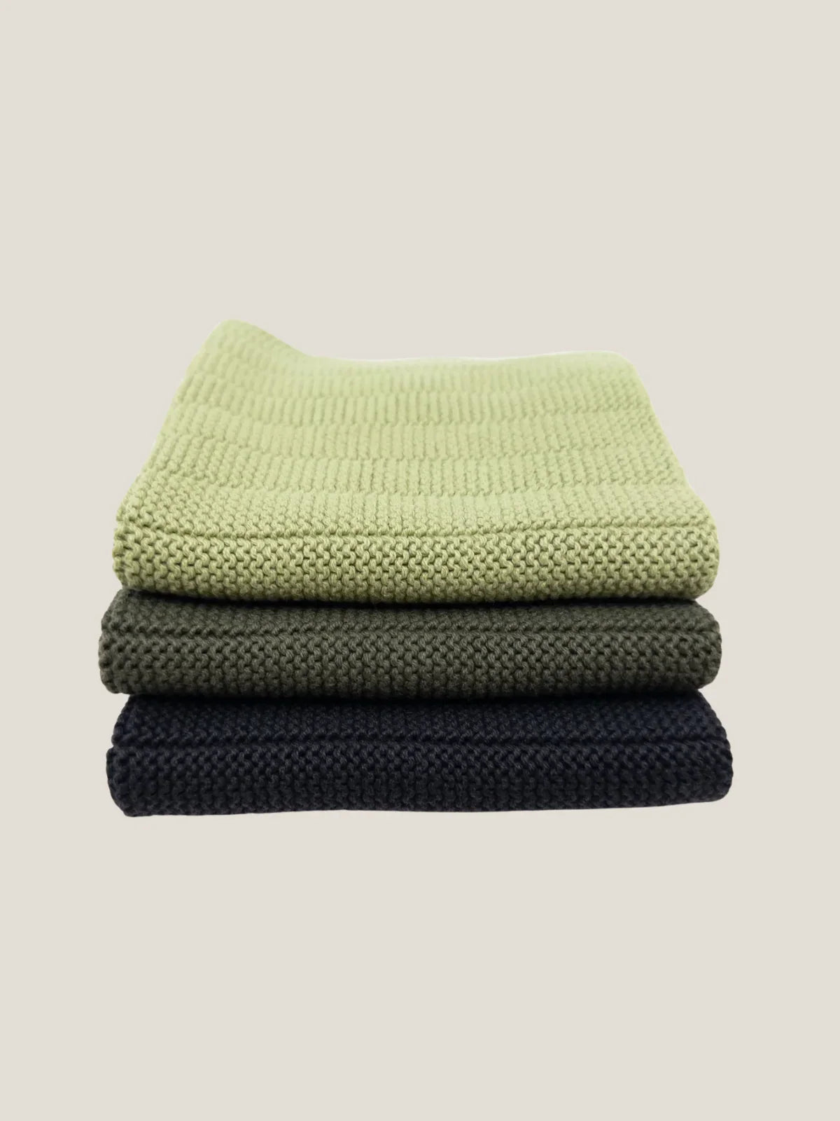Stack of three folded textured dishcloth in green, gray, and black on a beige background