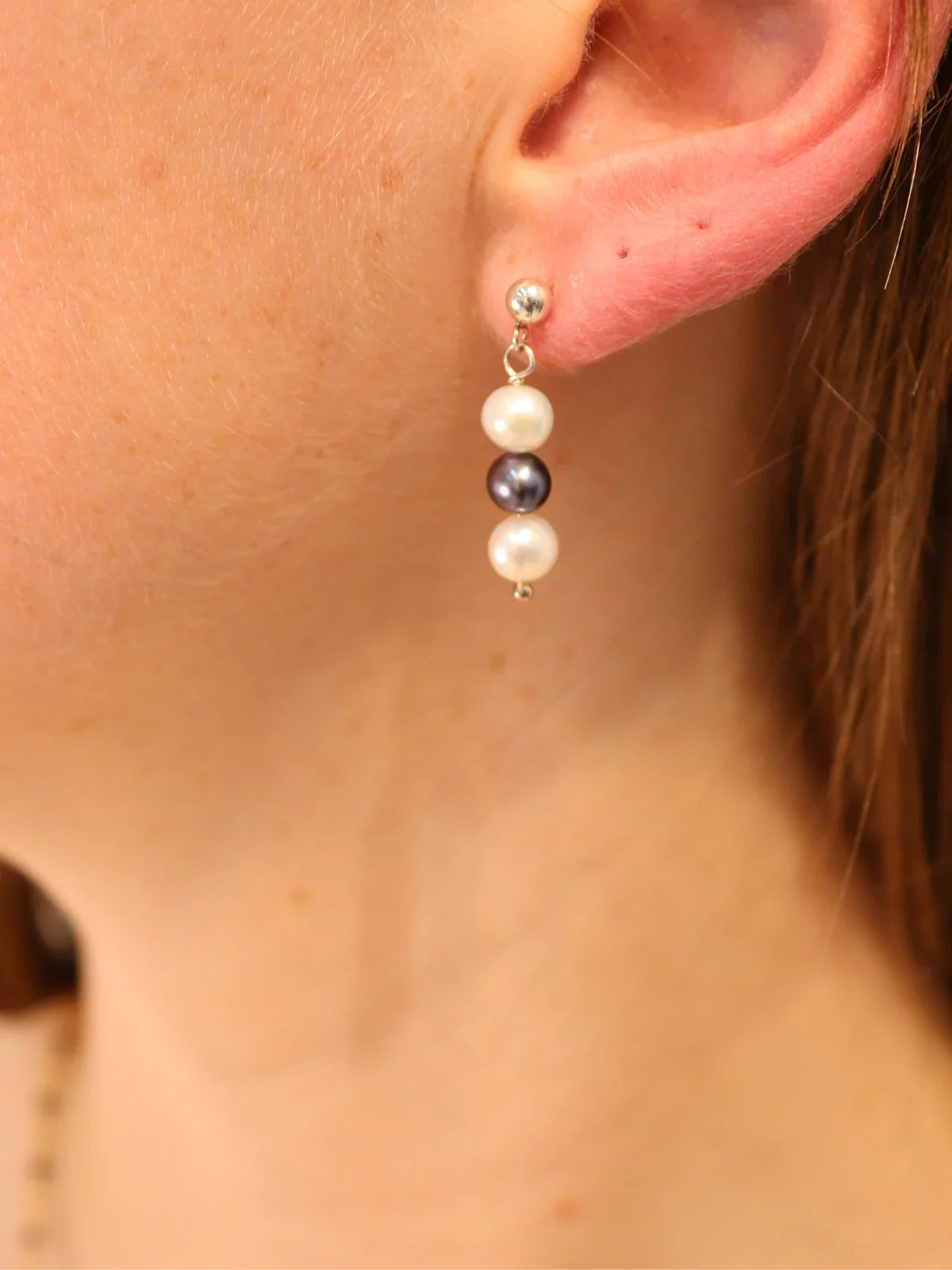 Close-up view of handcrafted triple pearl drop earrings featuring two white freshwater pearls and one black pearl on a silver setting.
