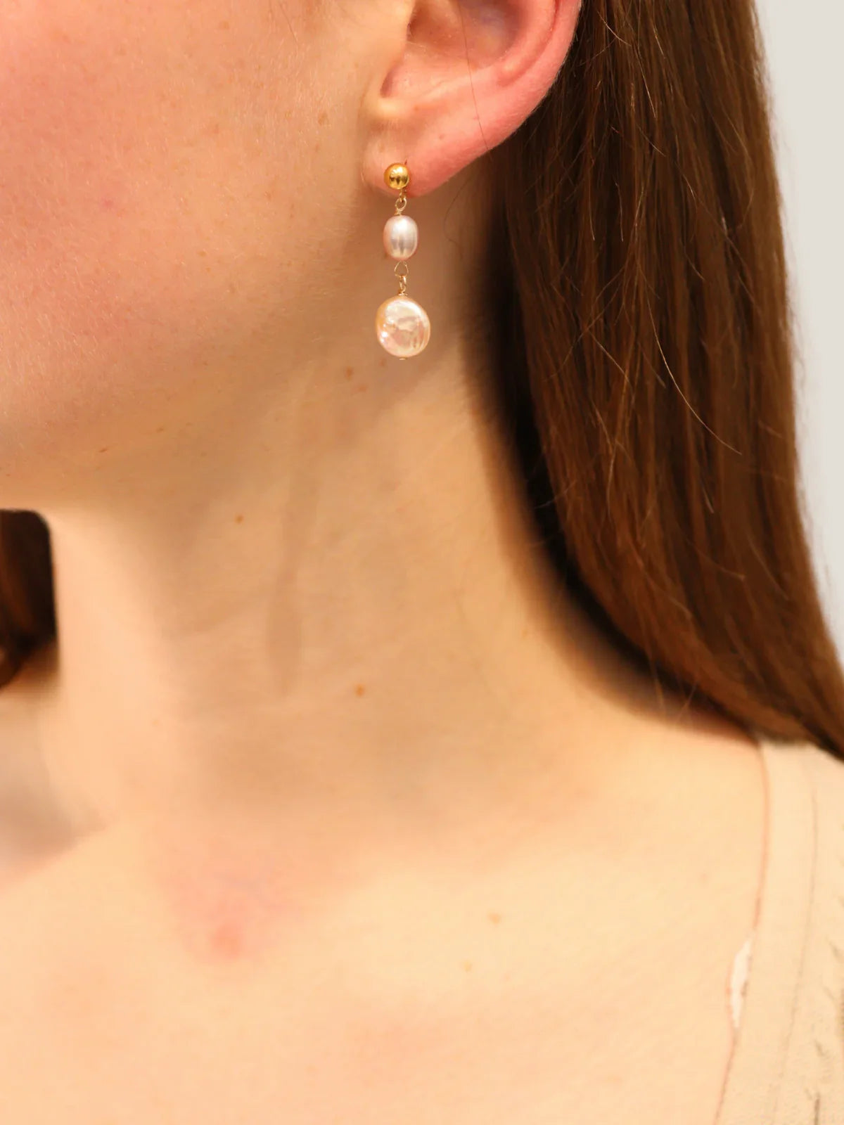 Close-up of a person wearing pearl drop earrings with a plain background