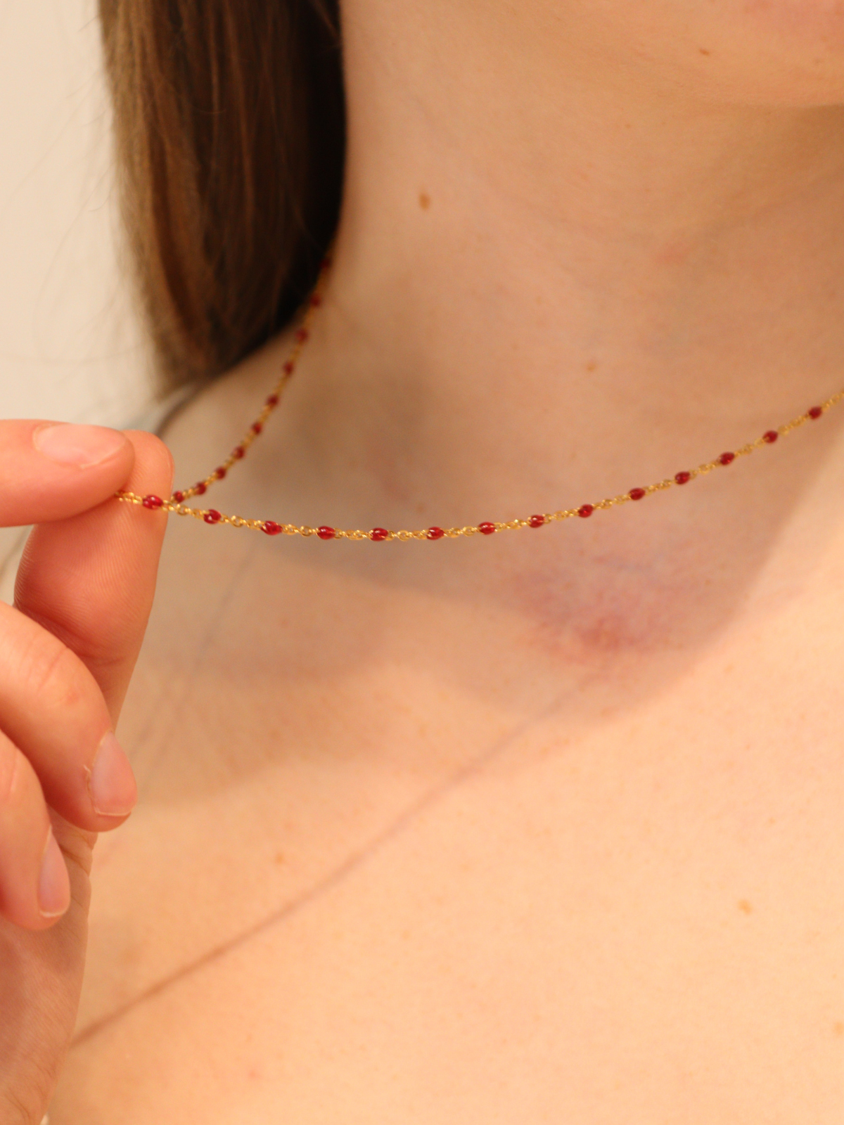 Delicate gold chain necklace with evenly spaced red beads, styled on neck.