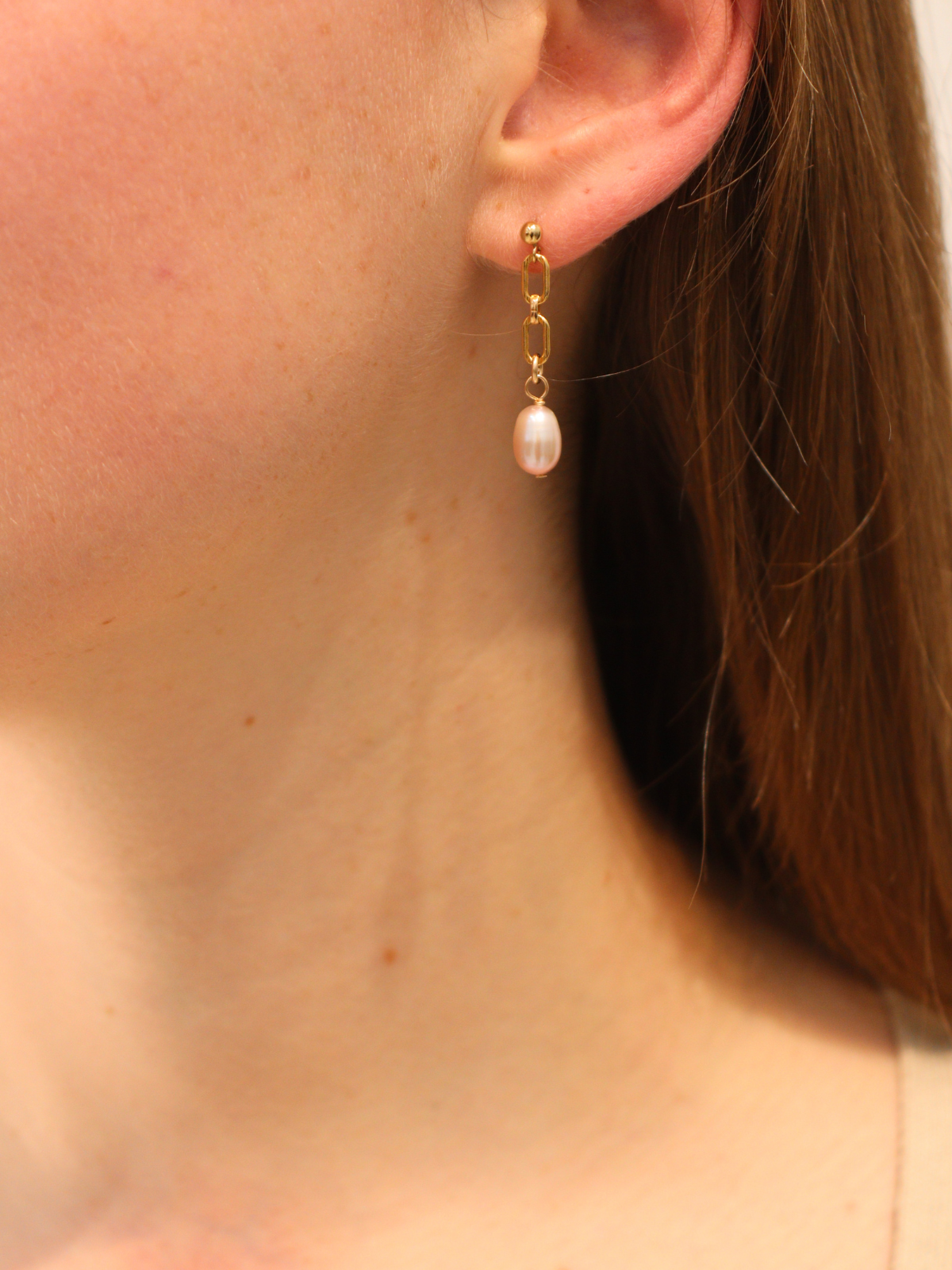 Gold chain link drop earring with a white pearl pendant, worn on ear.