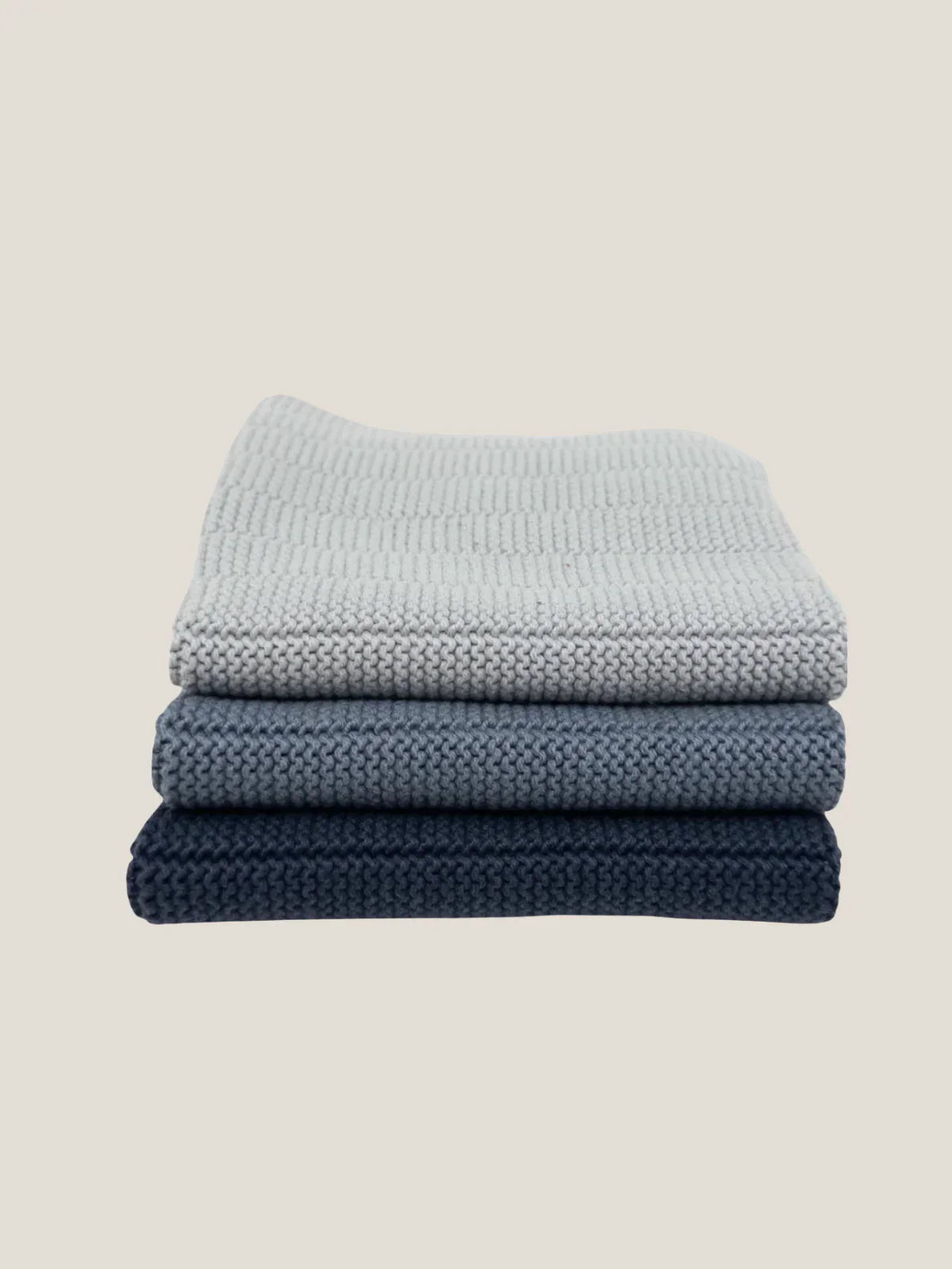 Stack of three folded textured cotton dishcloth in blue shades on a beige background