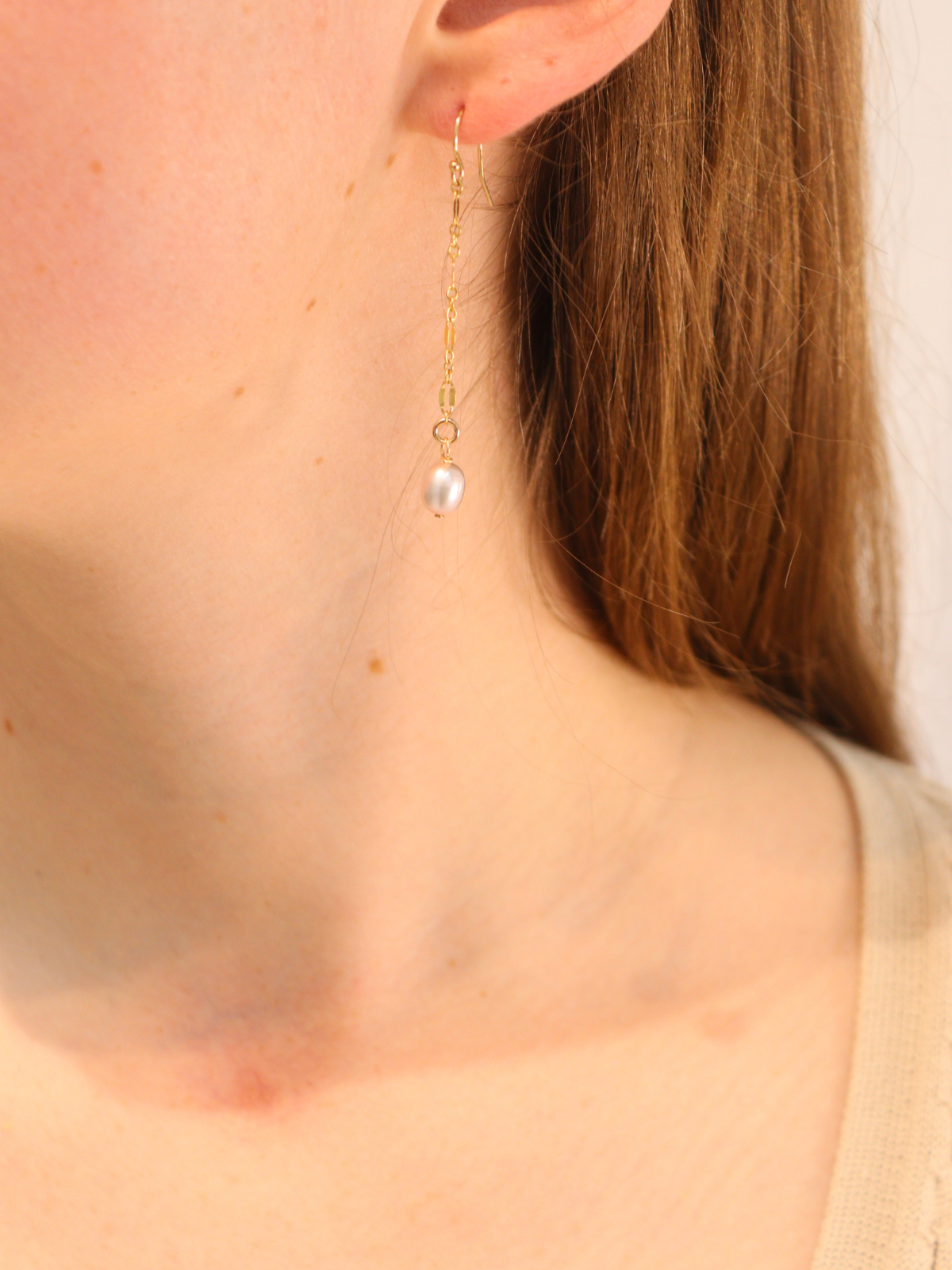 Gold chain drop earring with single white pearl, worn on ear.