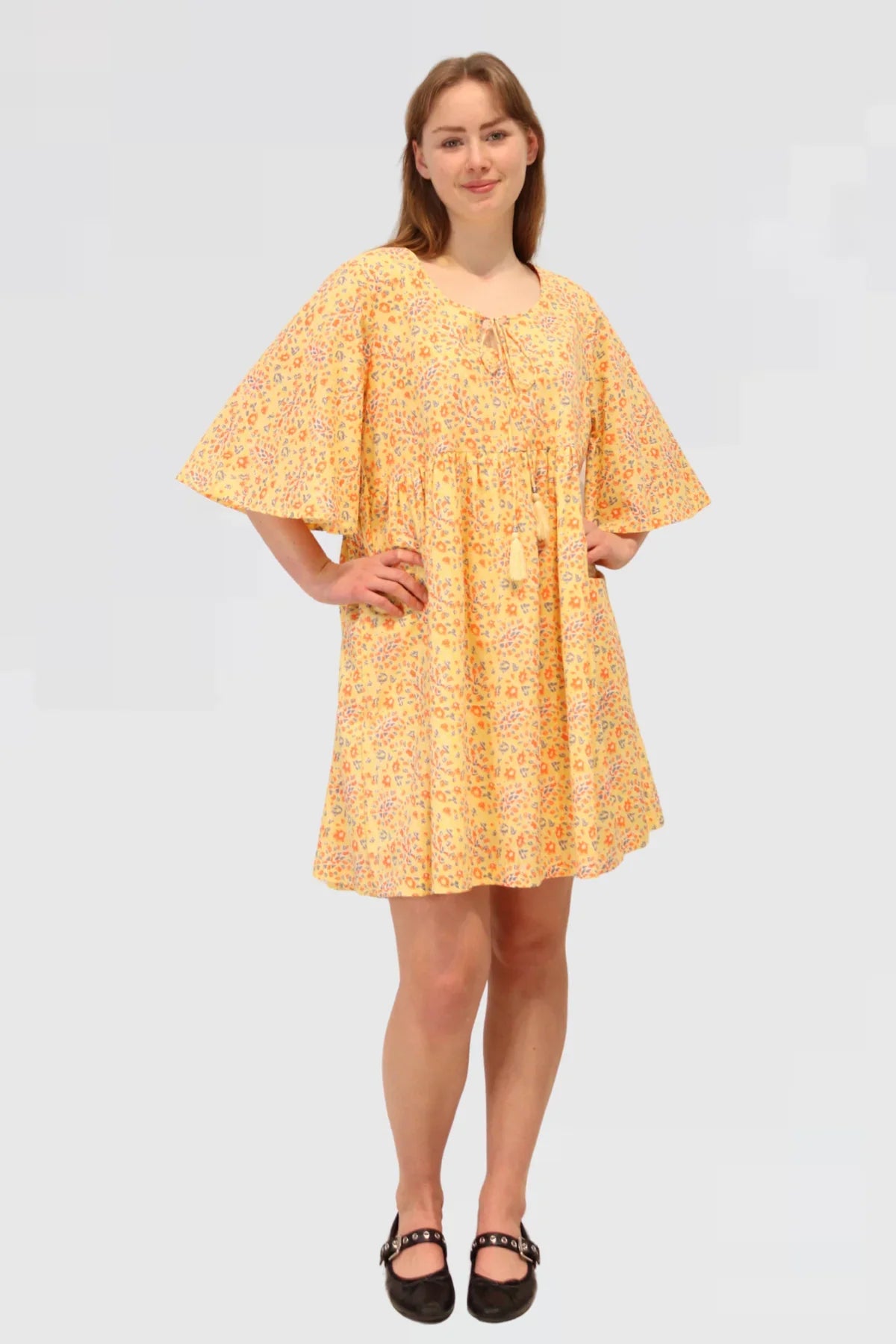 Woman wearing a yellow floral dress, Made ethically from 100% natural cotton on a plain background