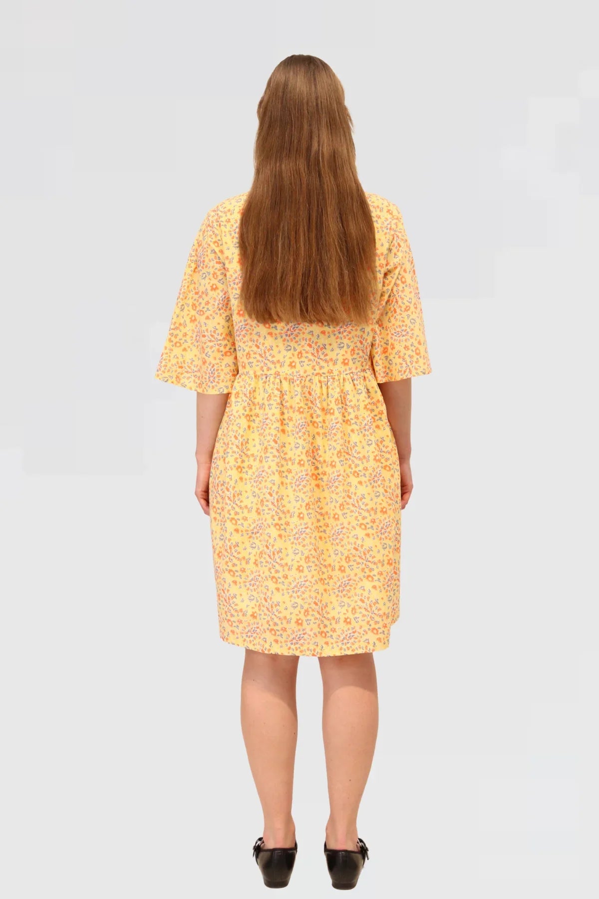 Woman wearing a yellow floral dress, Made ethically from 100% natural cotton on a plain background