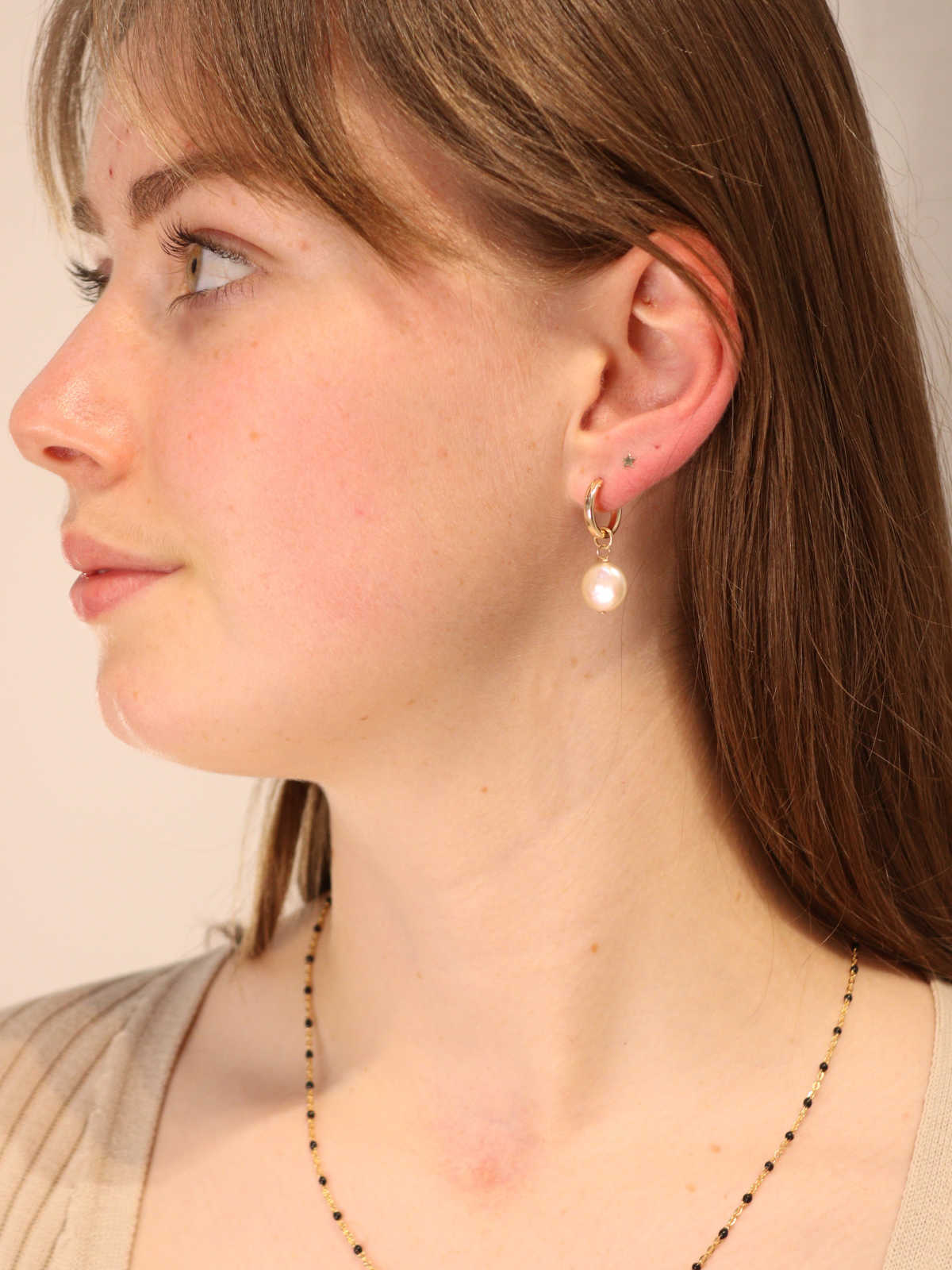 Woman wearing gold hoop earrings with dangling coin pearls.