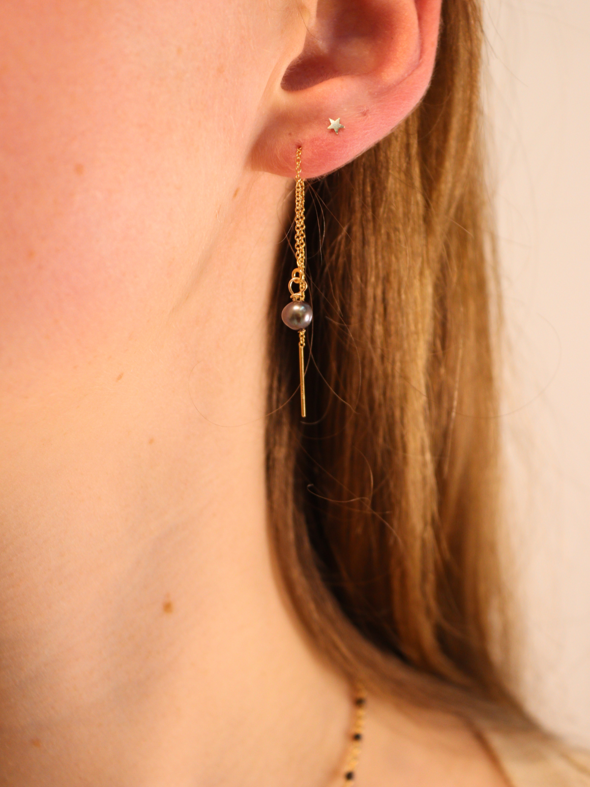 Gold threader earring with black pearl drop, styled with star stud.