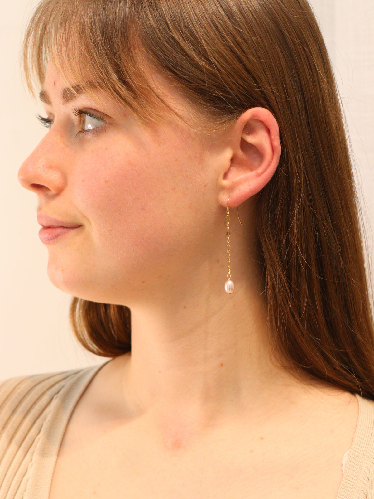 Delicate gold chain earring with dangling white pearl, close-up view on ear.