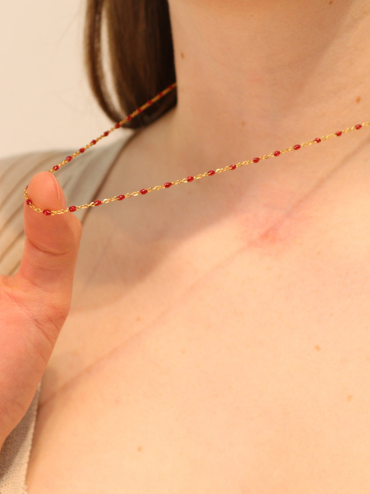 Gold chain necklace with small red beads, shown close-up while worn.