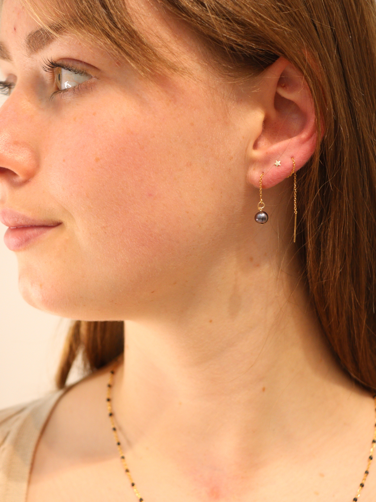 Delicate gold chain threader earring featuring a single black pearl.
