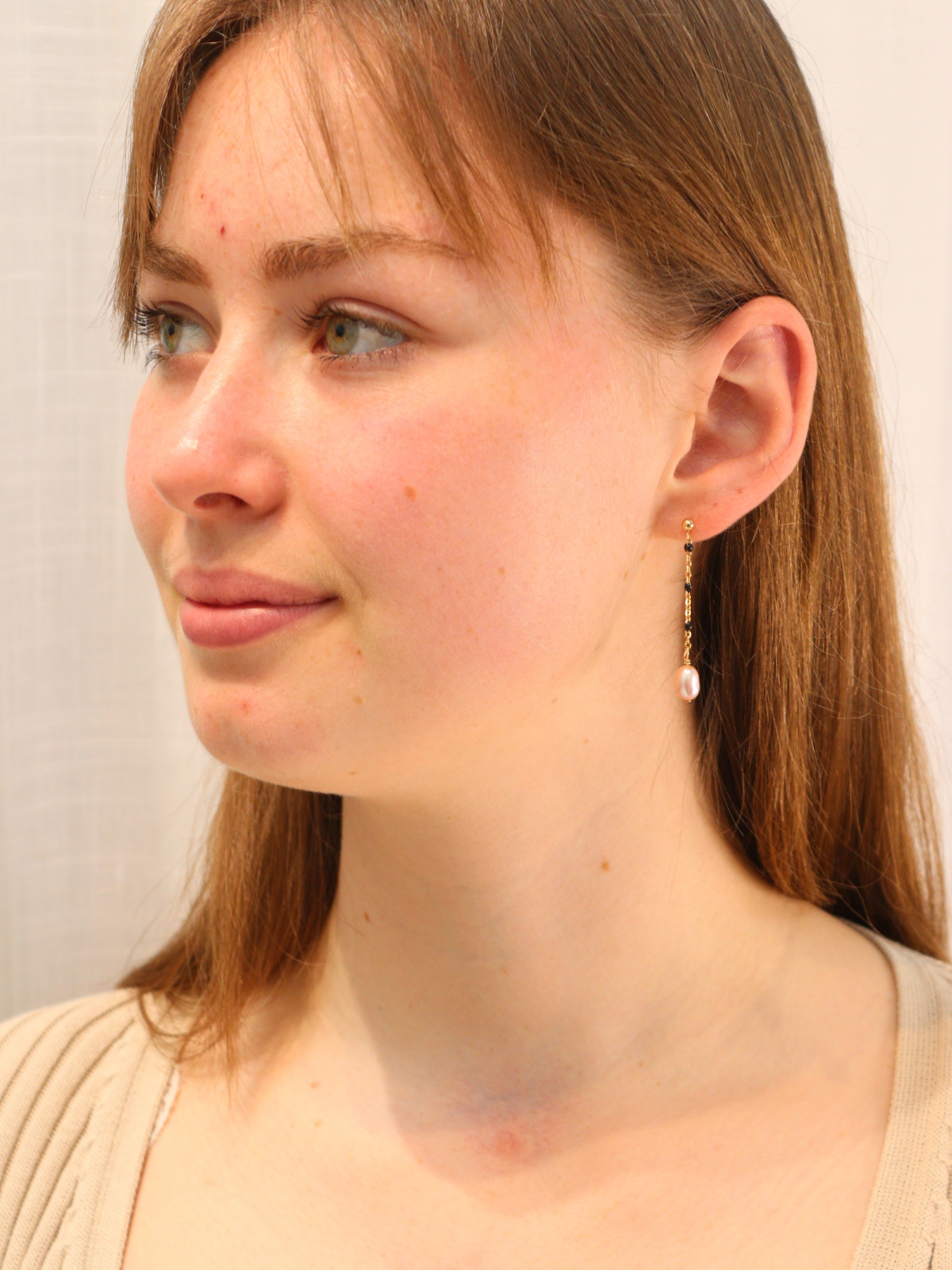 Woman wearing gold chain link pearl drop earrings, styled with neutral outfit.