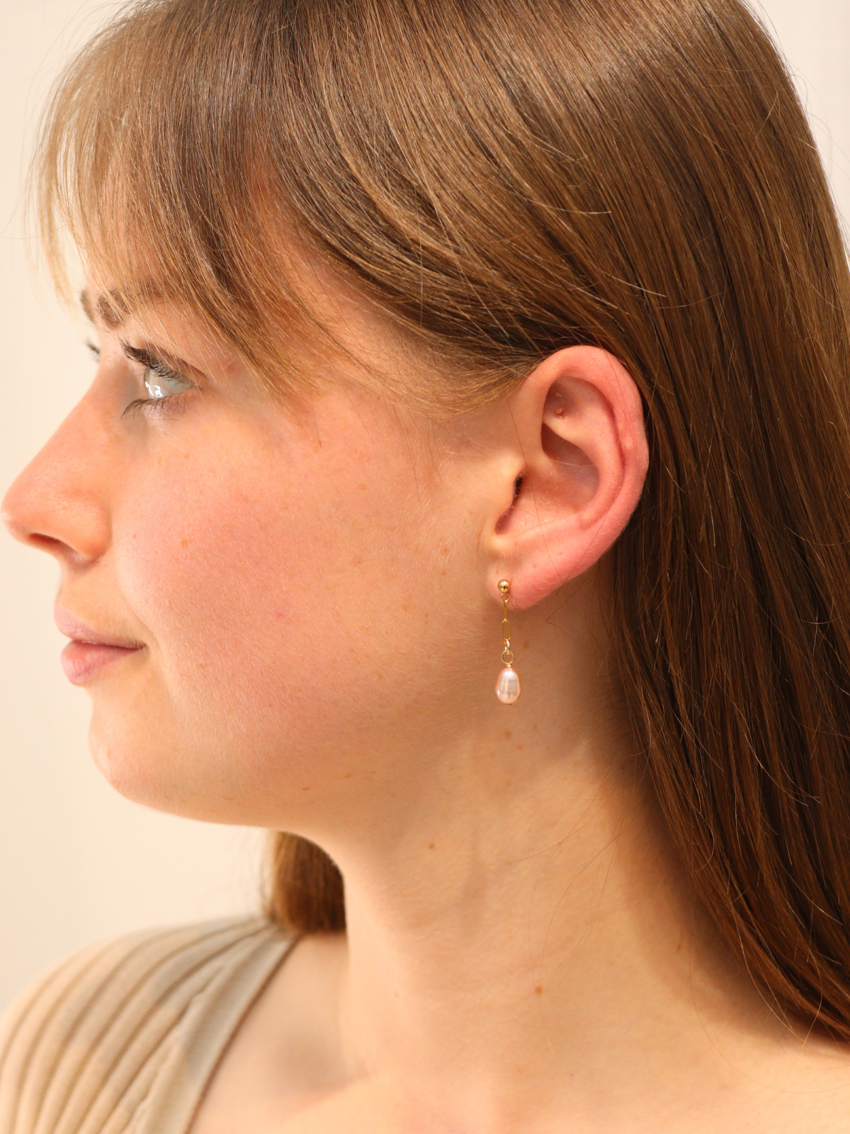 Woman wearing delicate gold drop earrings with teardrop pearl charms.