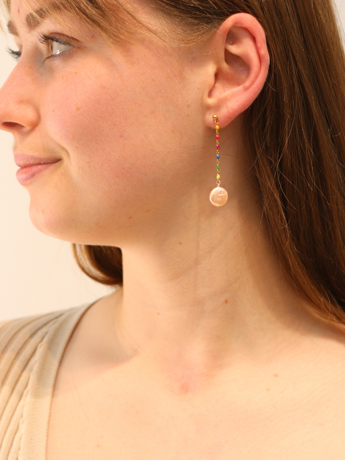 Woman wearing gold rainbow bead drop earrings with round pearl charm.