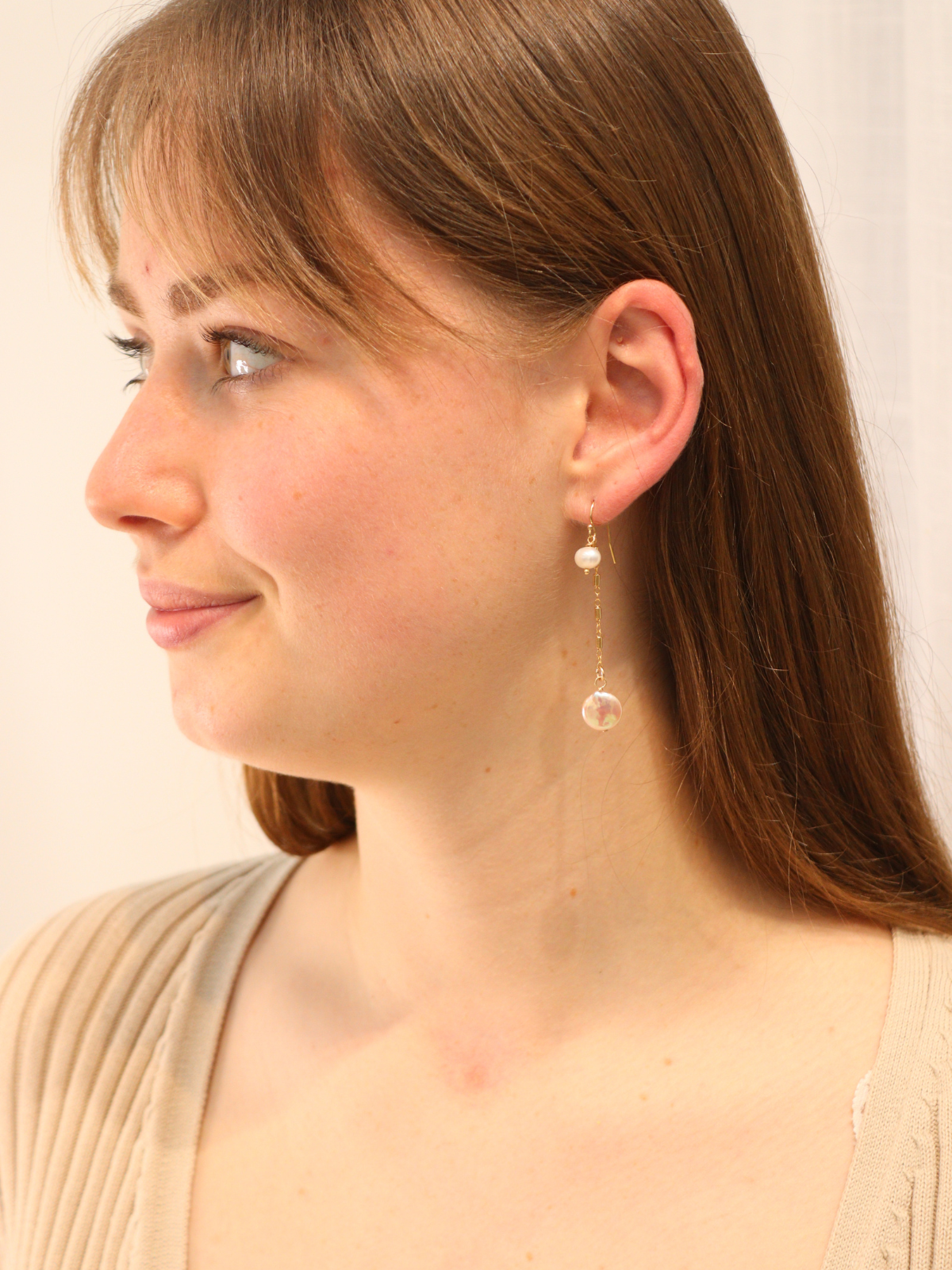 Woman wearing long gold drop earrings with double pearl accents.