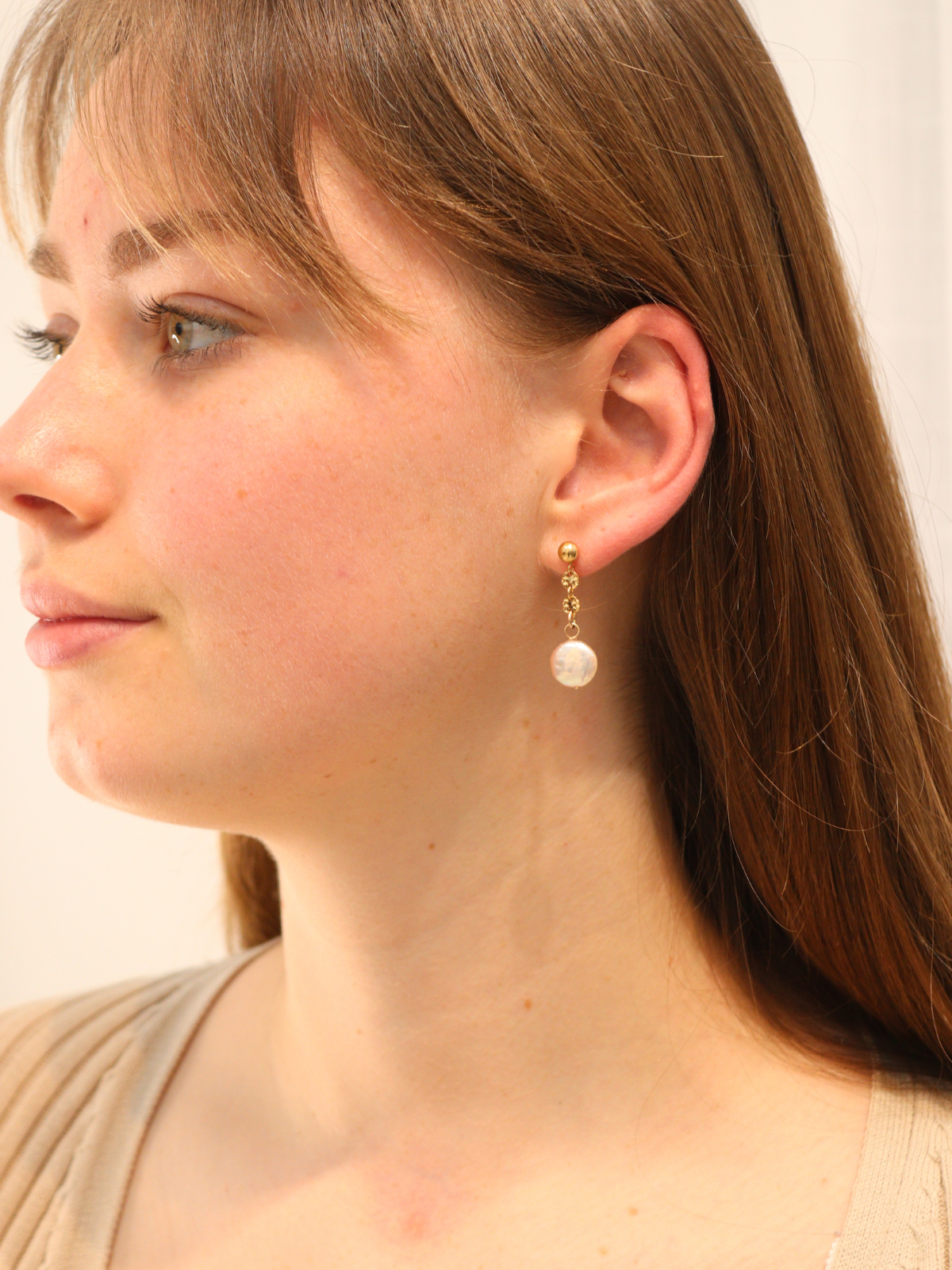Woman wearing classic gold pearl drop earrings.