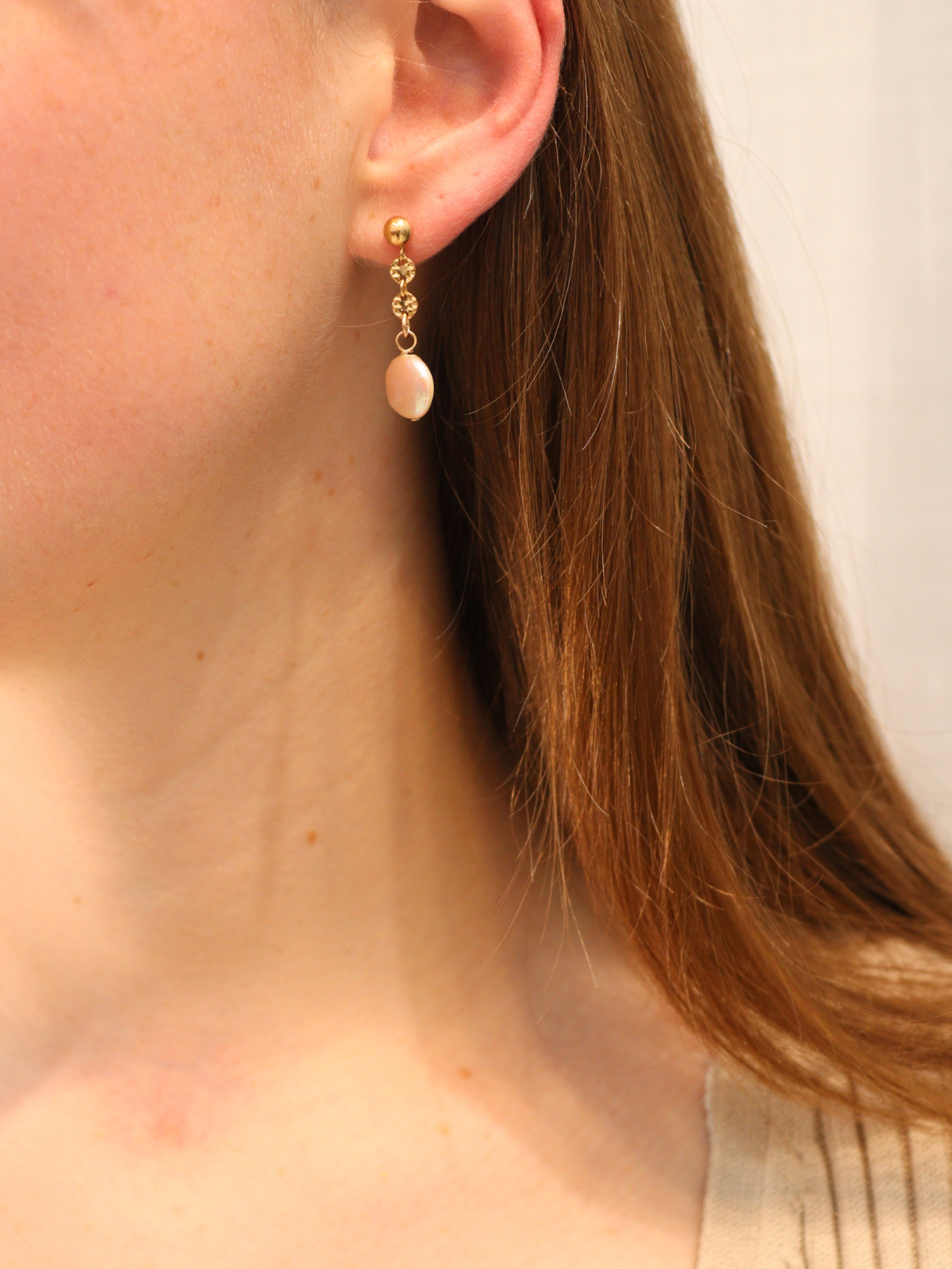 Gold drop earring with single round pearl, worn on ear.