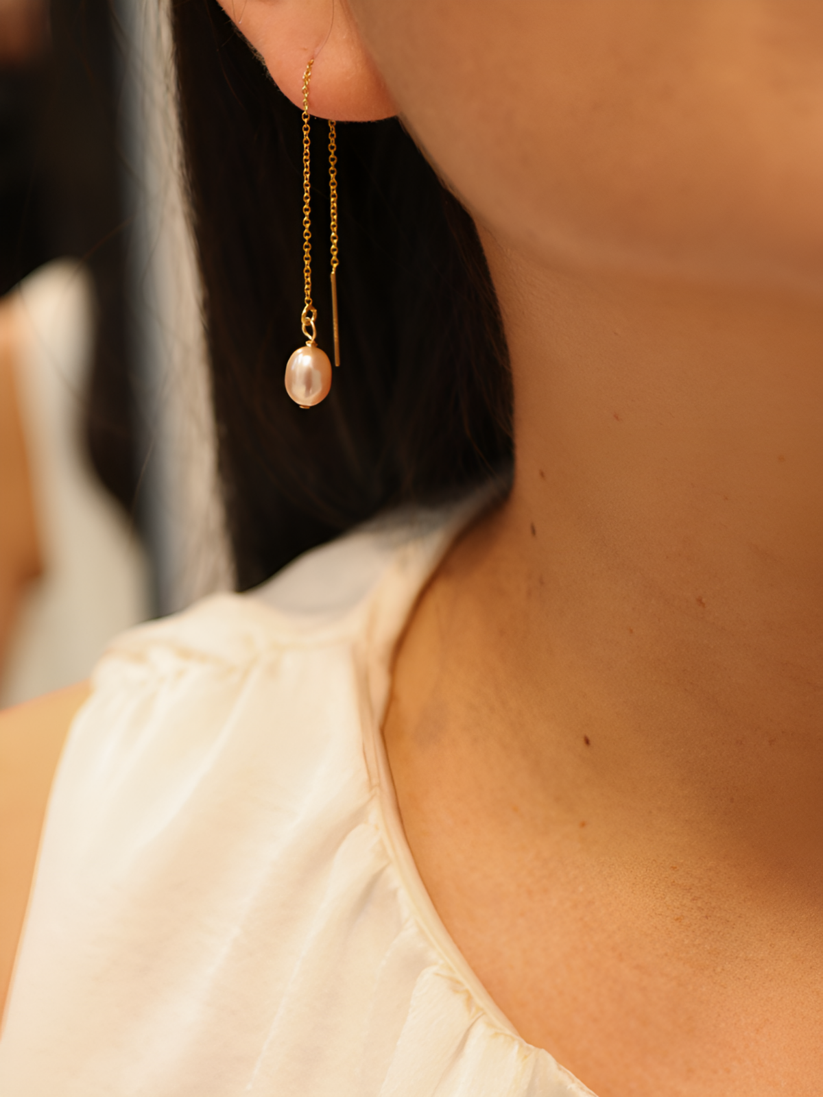 Close-up of a person wearing gold earrings with a pearl pendant.