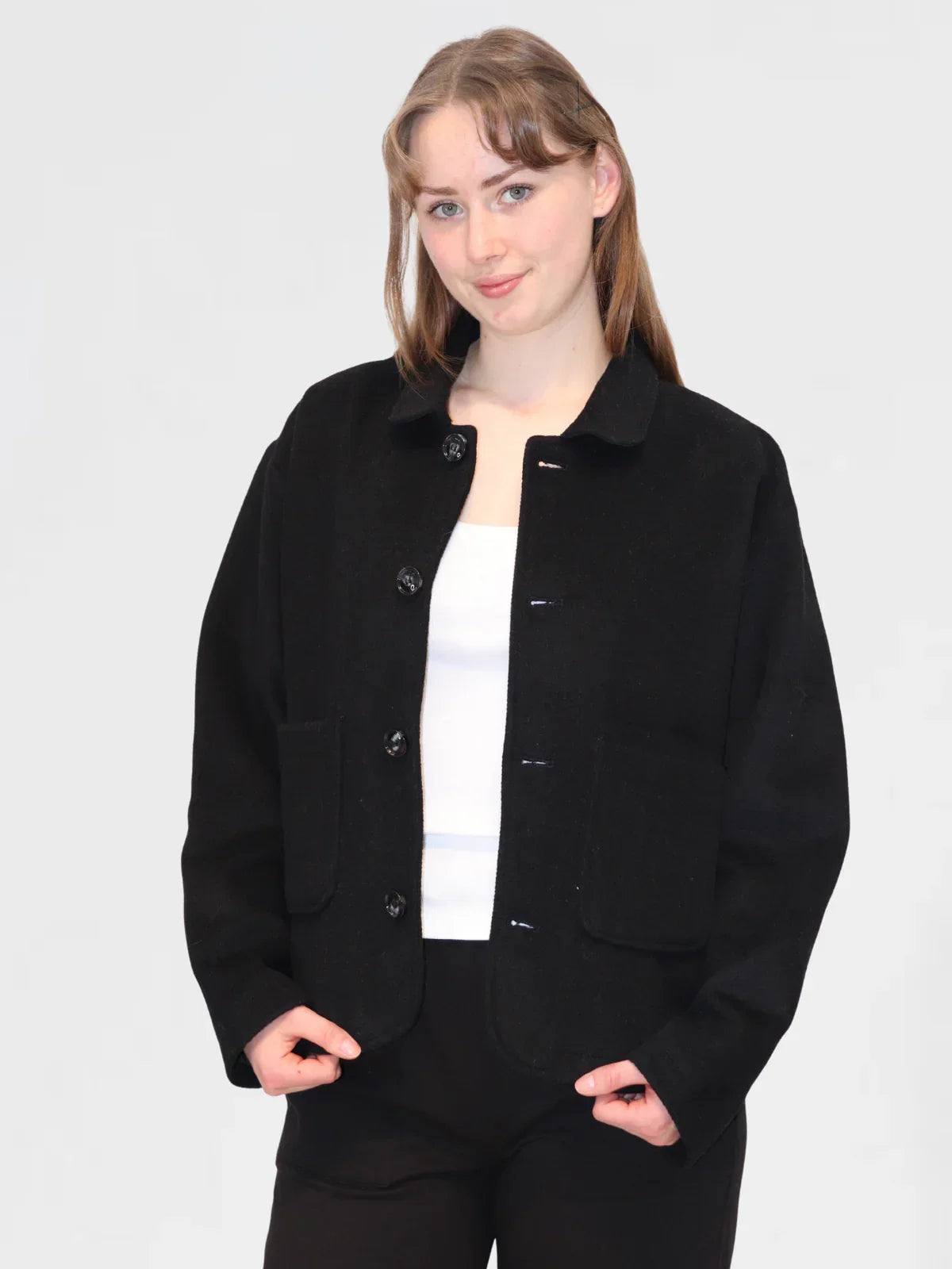 Woman wearing a black wool jacket over a white tank top on a plain background
