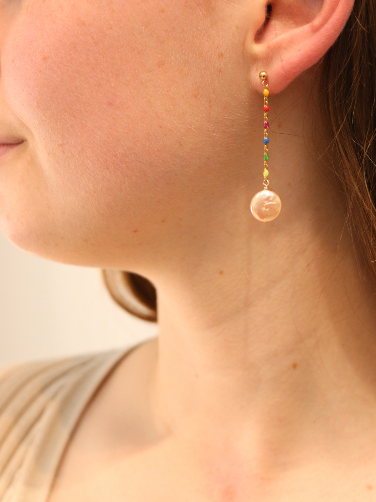 Colorful rainbow beaded gold drop earring with pearl pendant, shown on ear.
